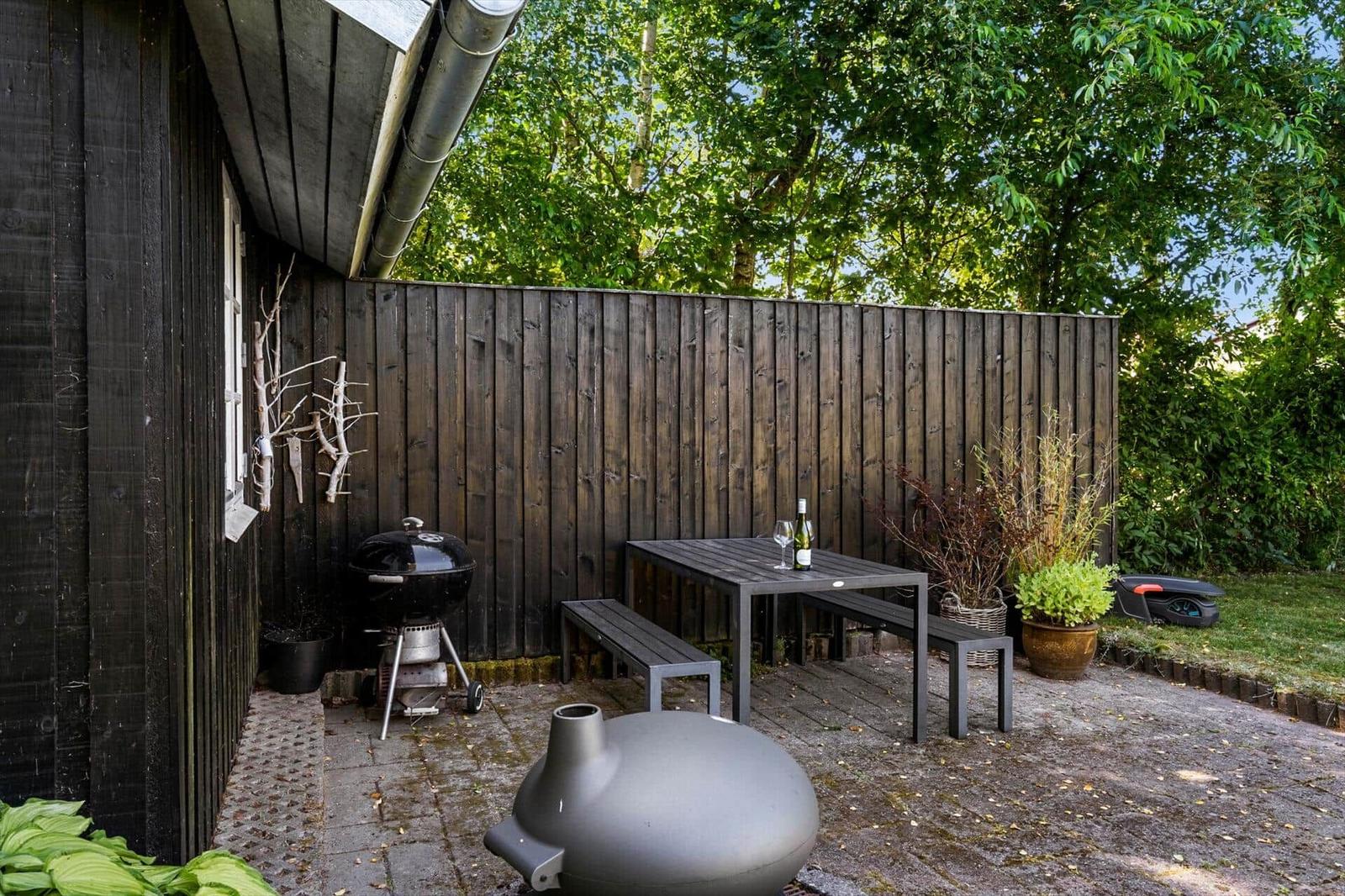 Hinterhof mit Tisch, Bänken, Grill und Pflanzen an Holzhauswand.