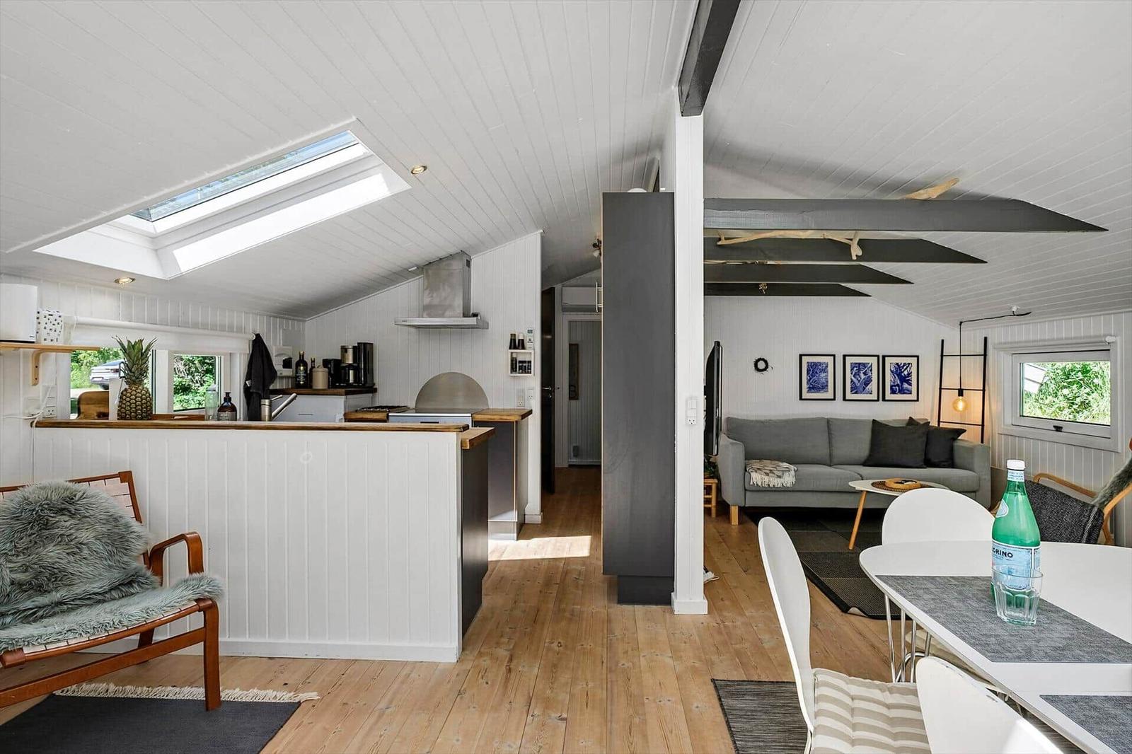 Wohnung mit Küche, Essbereich und Wohnzimmer. Holzboden, weiße Wände und Dachfenster.