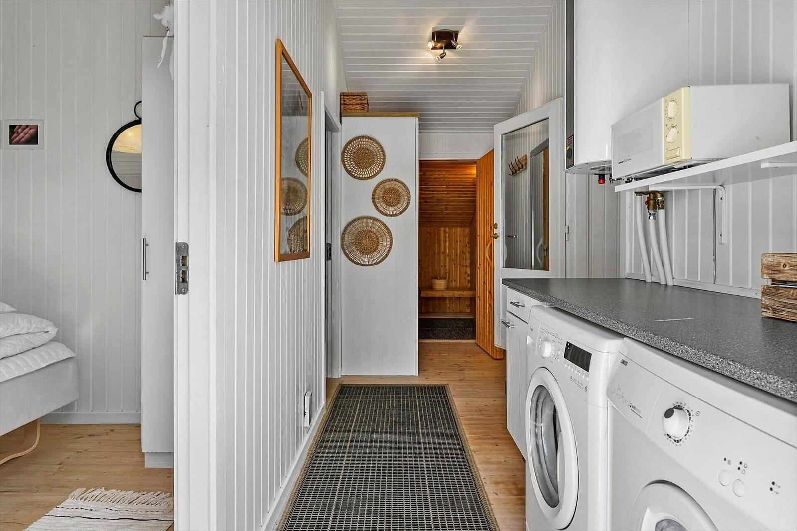 Flur mit Waschmaschine, Sauna und Schlafzimmer. Weiße Wände, Holzboden und Küchengeräte.