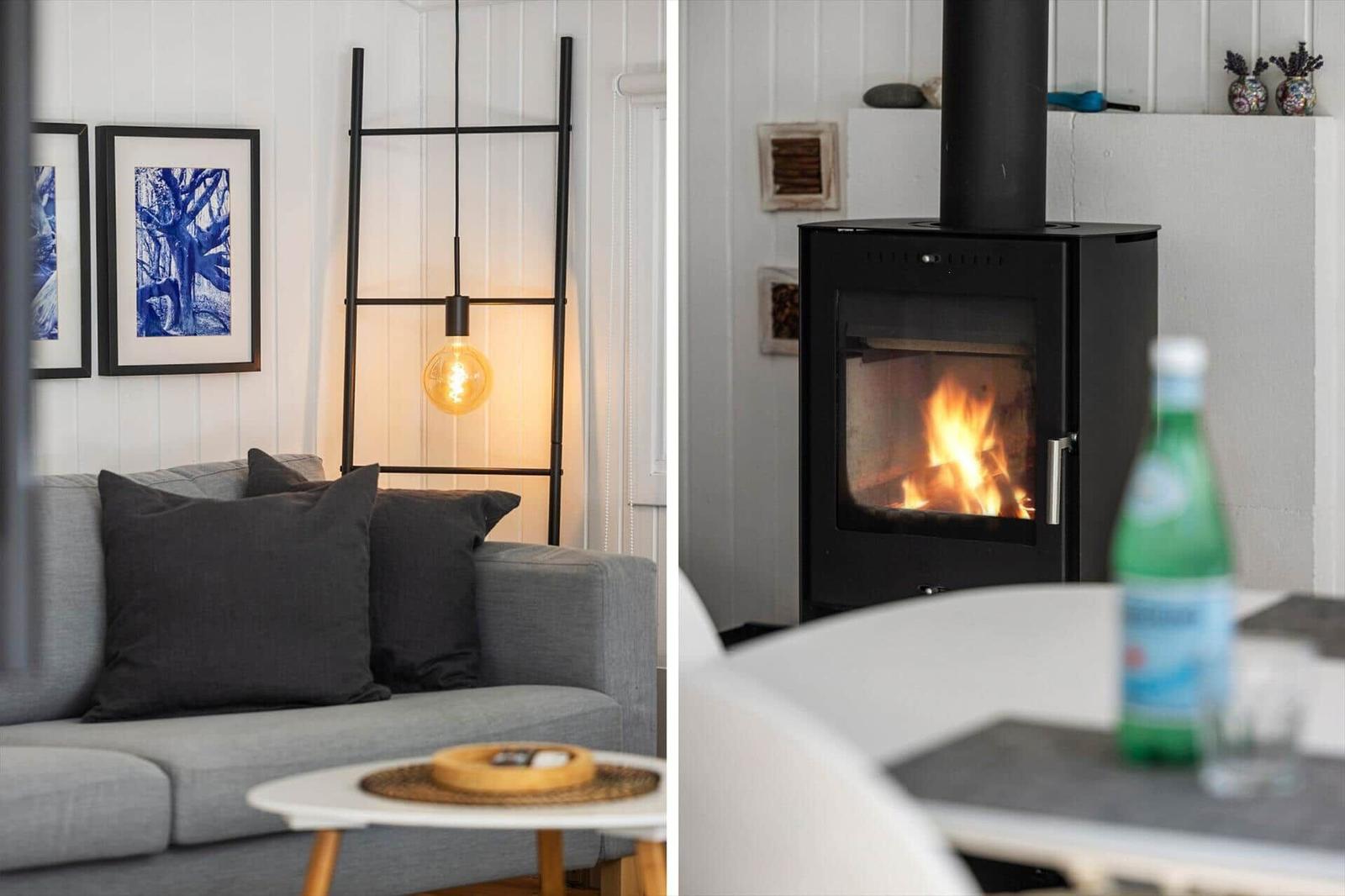 Ein grauer Sofa mit Kissen, eine Hängelampe und ein Kamin mit brennendem Feuer.
