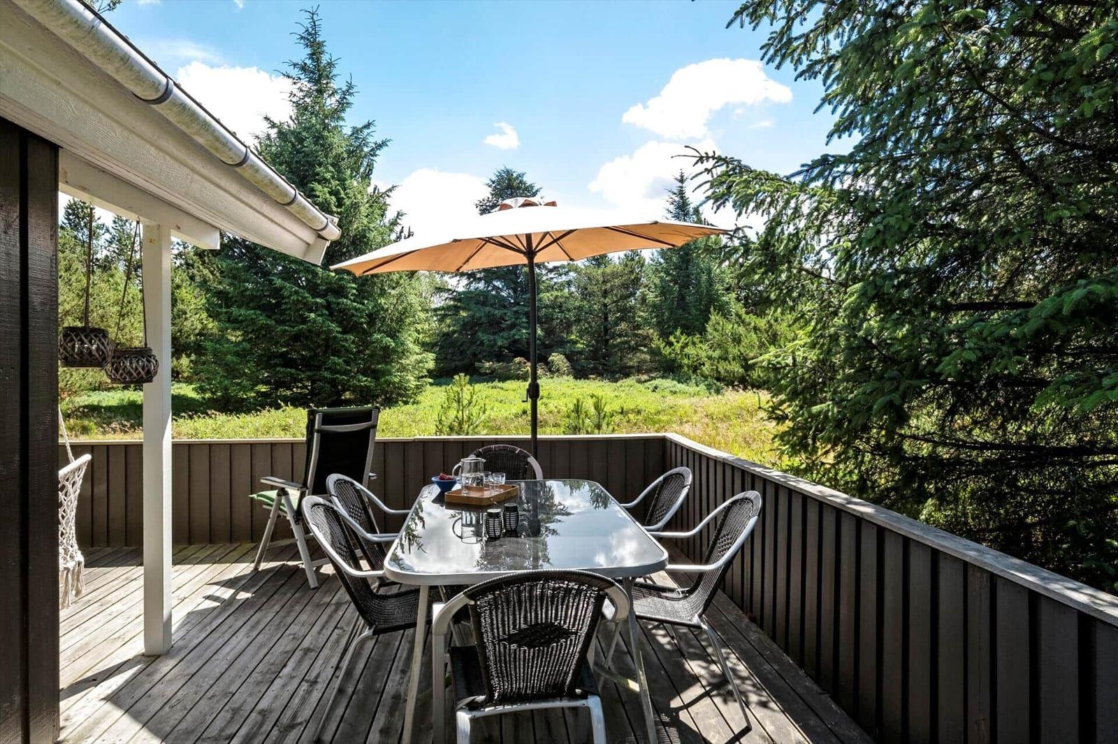 Terrasse mit Tisch, Stühlen und Sonnenschirm. Blick in einen grünen Wald.