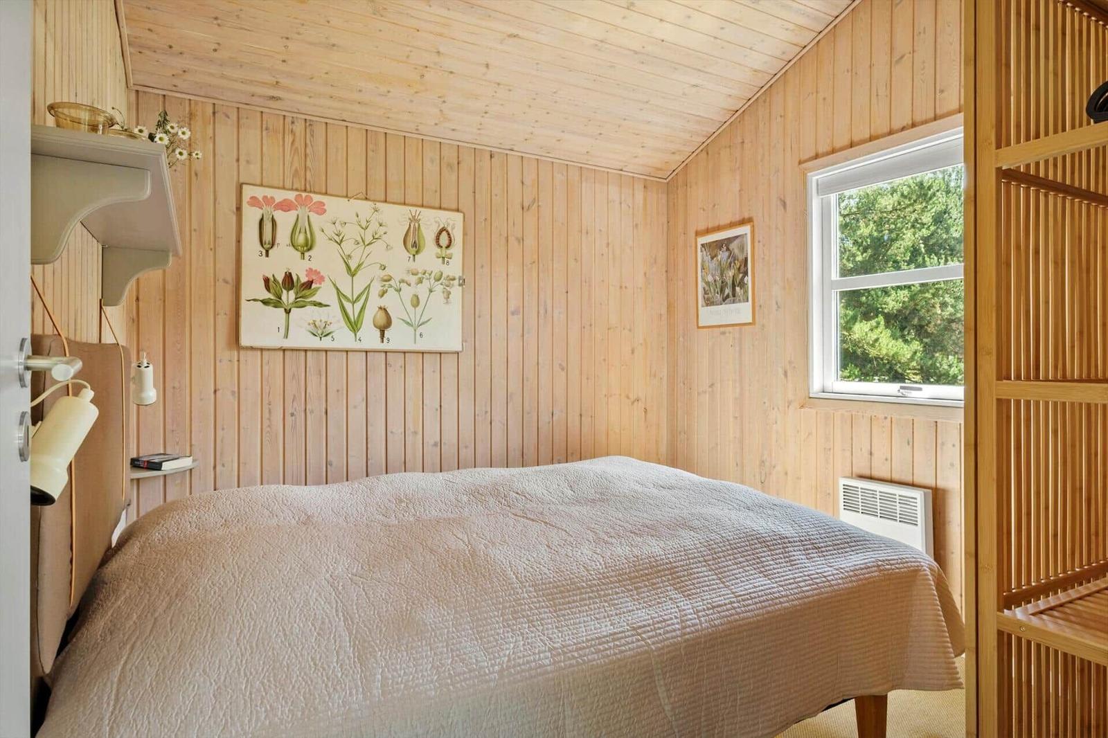 Schlafzimmer mit Holzwandverkleidung, Bett und Fenster mit Blick auf Grün.