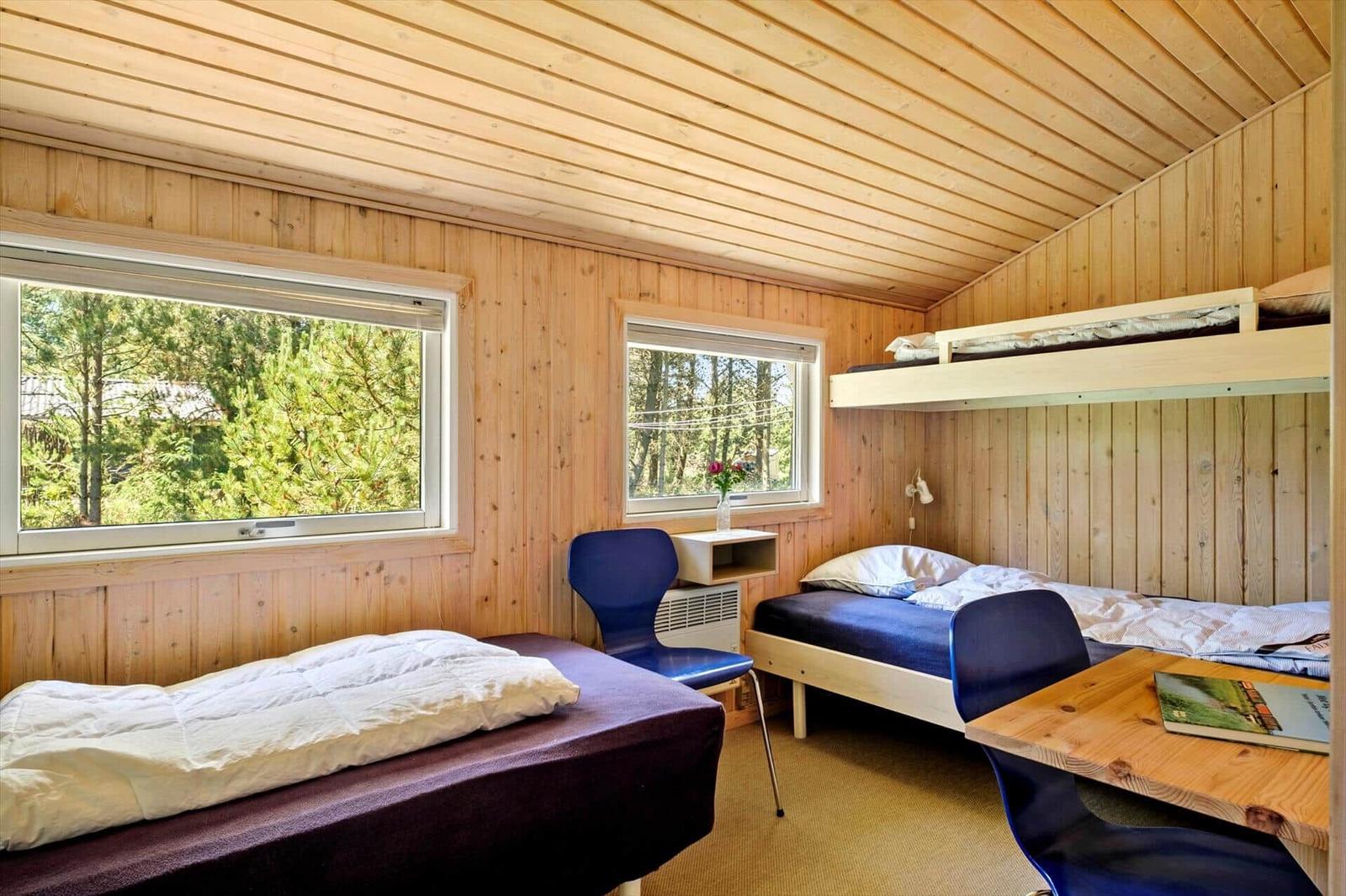 Zimmer mit Holzwand, zwei Betten und Tisch. Fenster zeigen Wald.