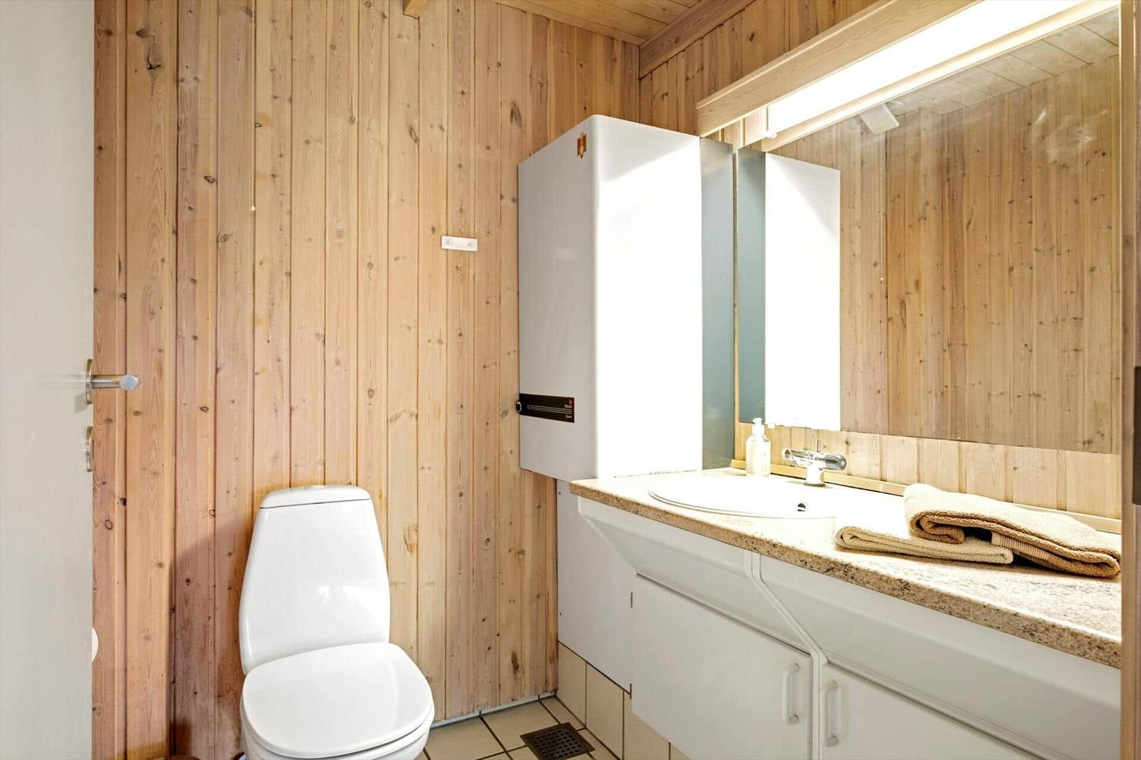 Badezimmer mit Holzwand, Toilette, Waschbecken und Spiegel