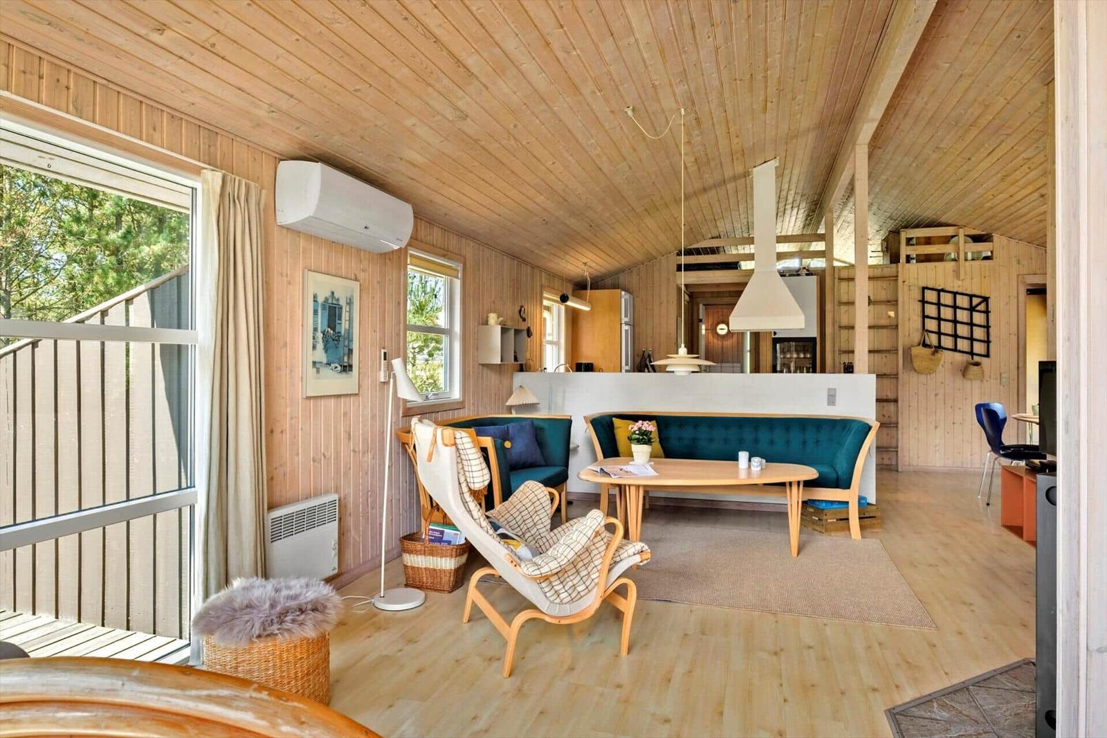 Wohnraum mit Holzdecke, blauem Sofa und Holzmöbeln. Fenster und Balkon sichtbar.