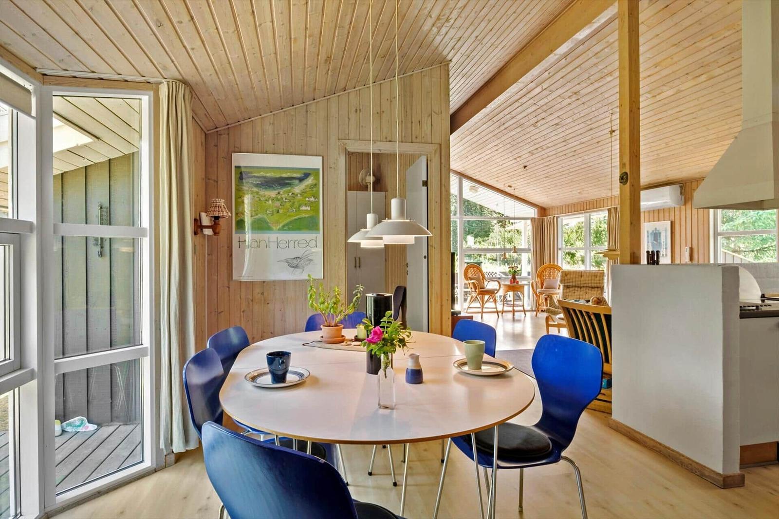 Essbereich mit runden Tisch und blauen Stühlen, Holzwände und große Fenster.