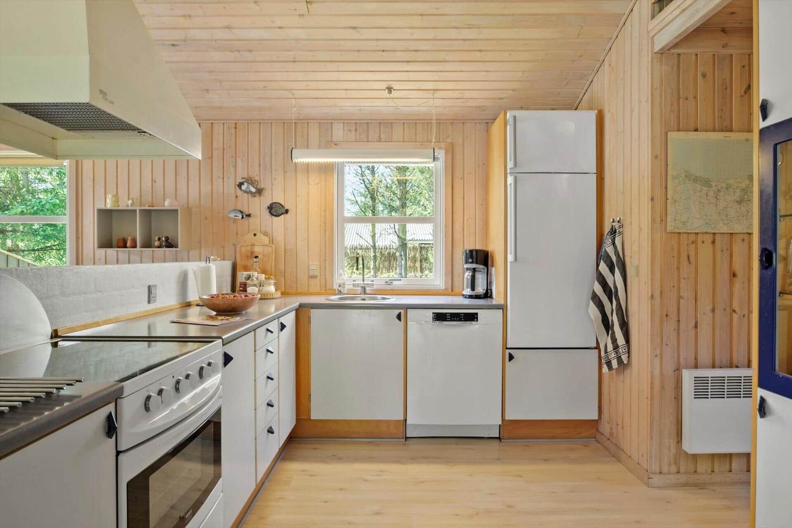 Küche mit Holzwand, Kühlschrank, Spüle und Fenster.