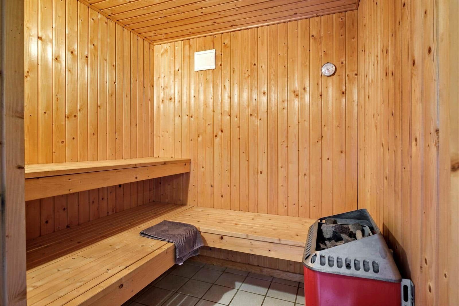 Sauna mit Holzwand und Sitzbänken, Heizung und Thermometer sichtbar.
