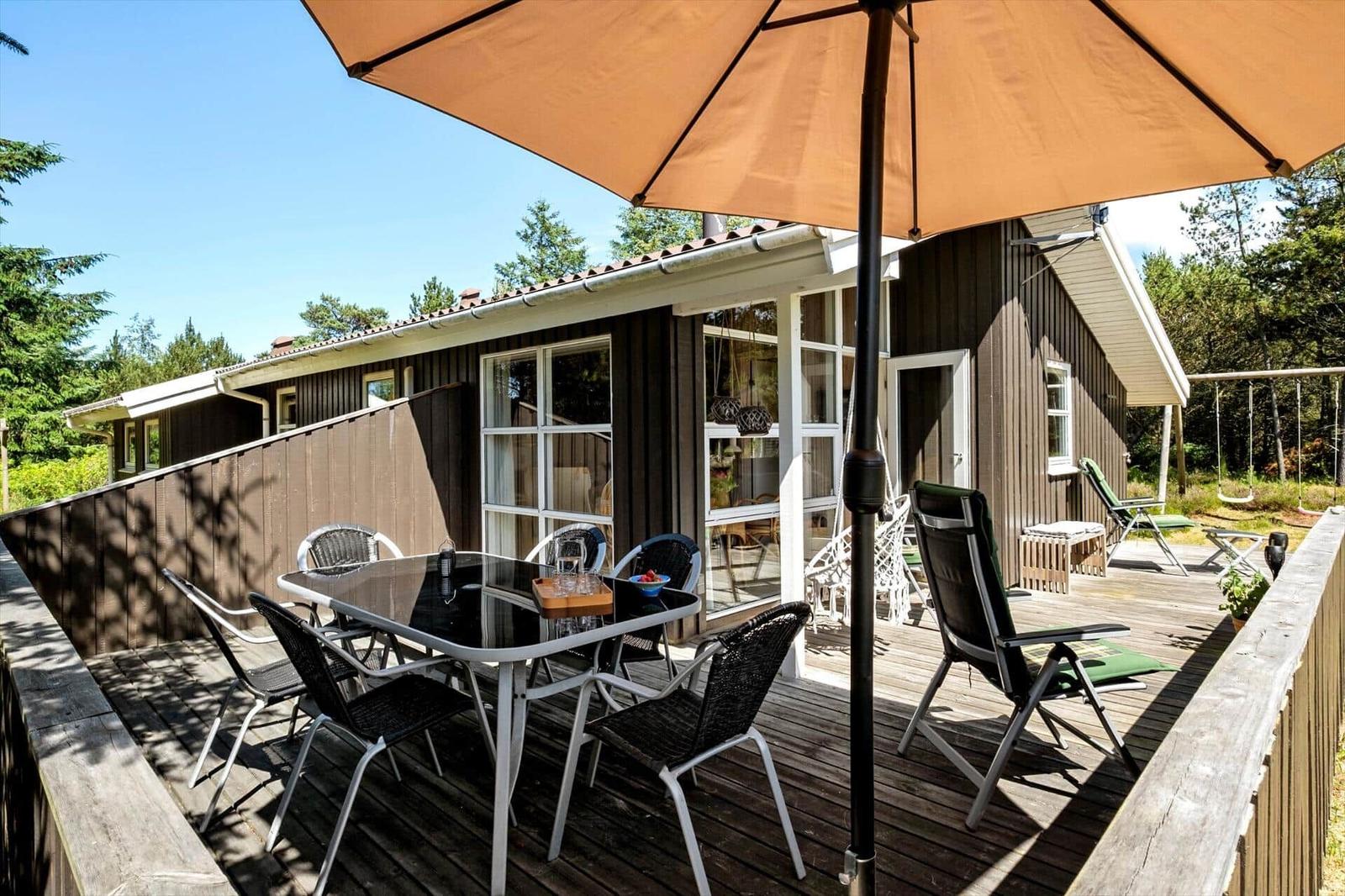 Terrasse mit Tisch, Stühlen und Sonnenschirm vor einem Haus mit Holzfassade.