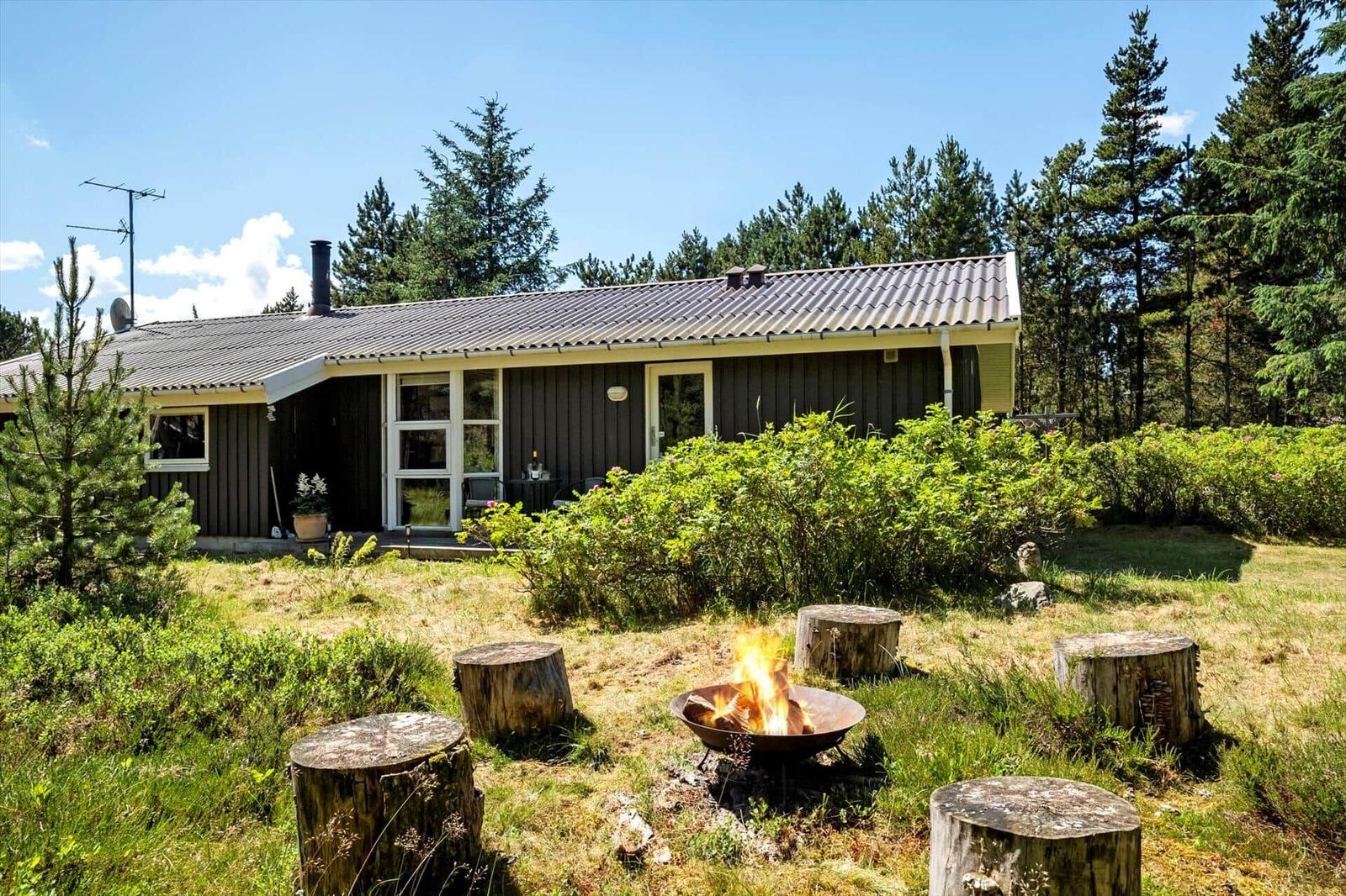 Ein Haus mit Garten und Feuerkorb. Im Hintergrund sind Bäume zu sehen.