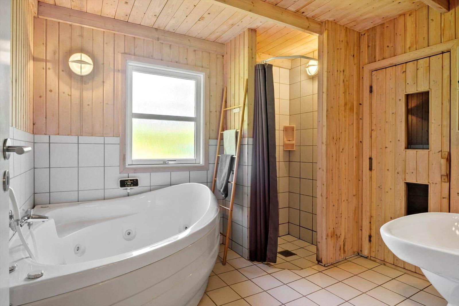 Bad mit Whirlpool, Dusche und Waschbecken. Holzwände und Fenster mit Blick.