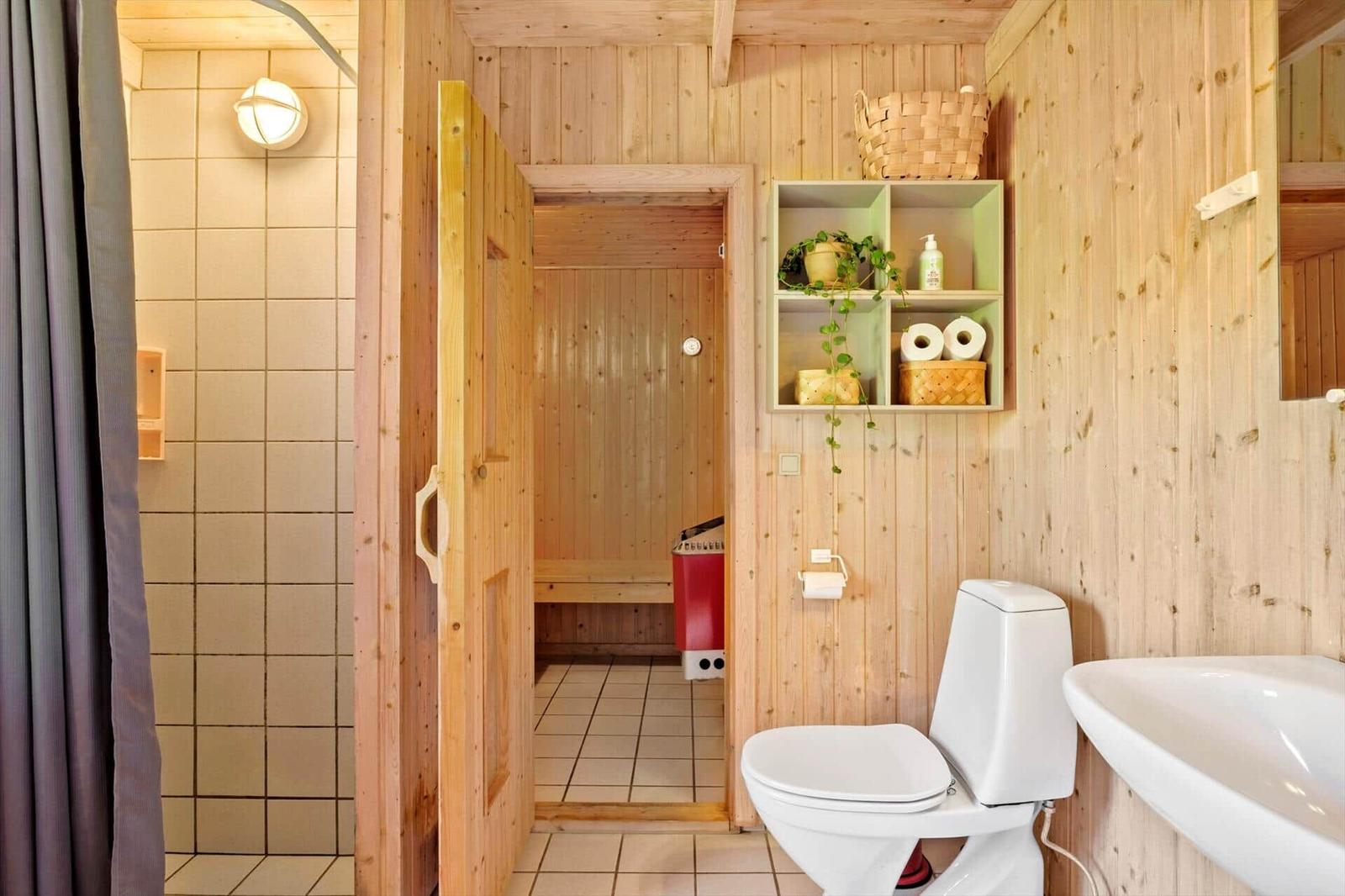 Bad mit Dusche, Toilette und Waschbecken. Sauna im Hintergrund.