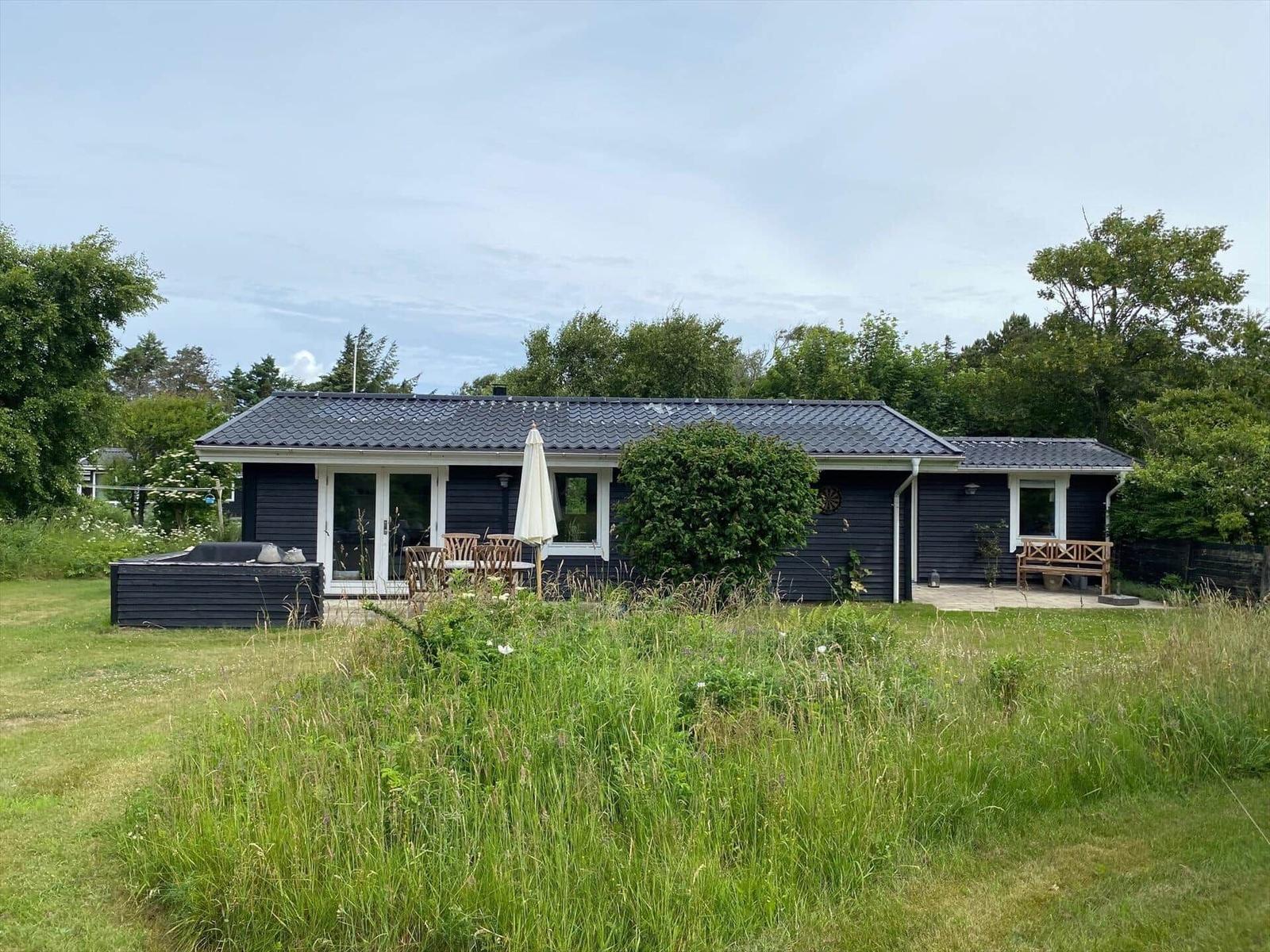 Ein dunkelblaues Ferienhaus mit Garten, Terrasse und Sonnenschirm.