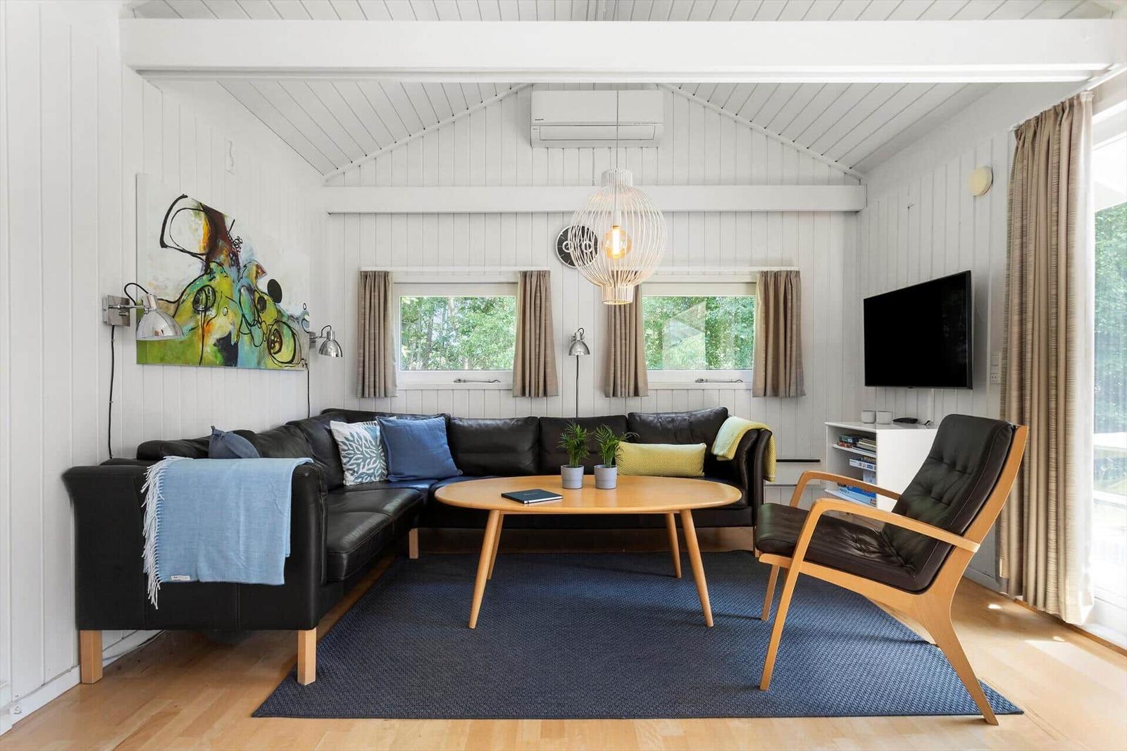 Ein Wohnzimmer mit schwarzer Sofa, Holztisch und Fernseher an der Wand.