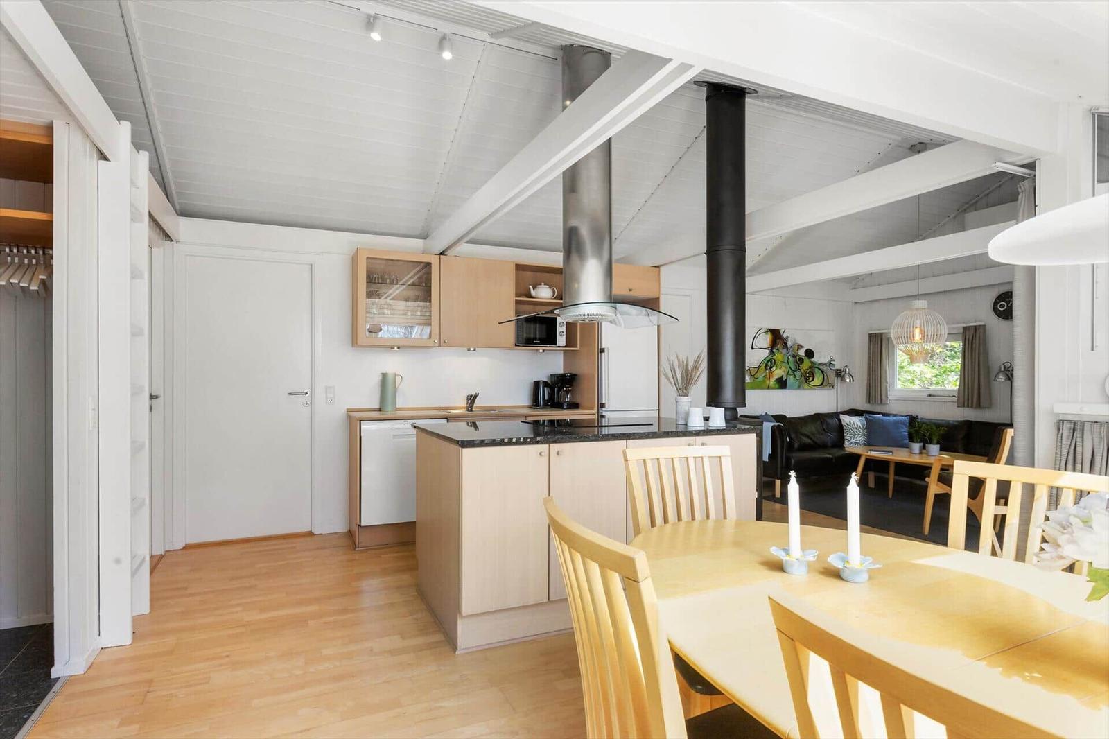 Küche mit Essbereich und Wohnzimmer im Hintergrund. Holzfußboden und weiße Decken.