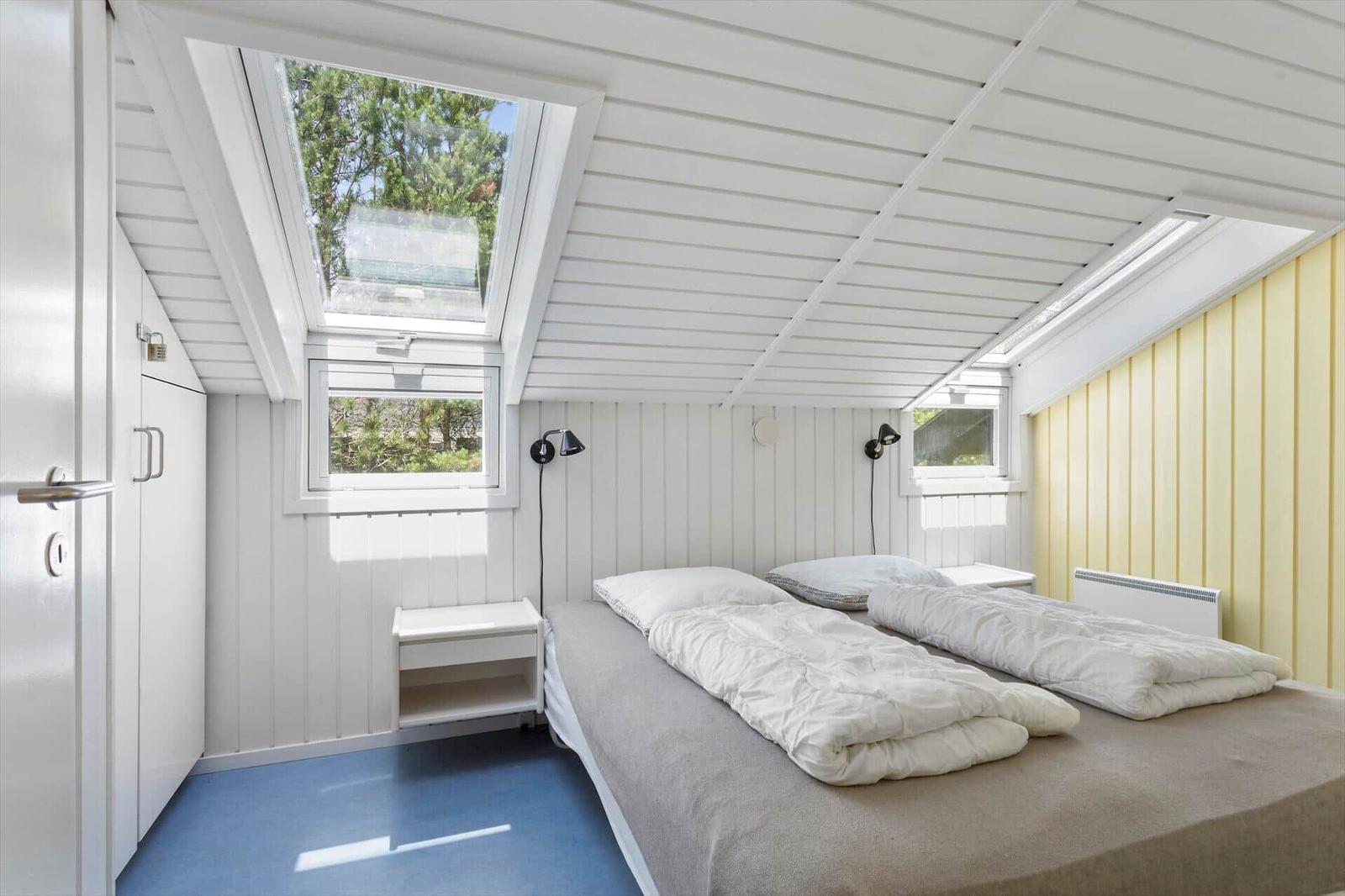 Schlafzimmer mit Doppelbett, Dachfenster und gelbem Wandpaneel.