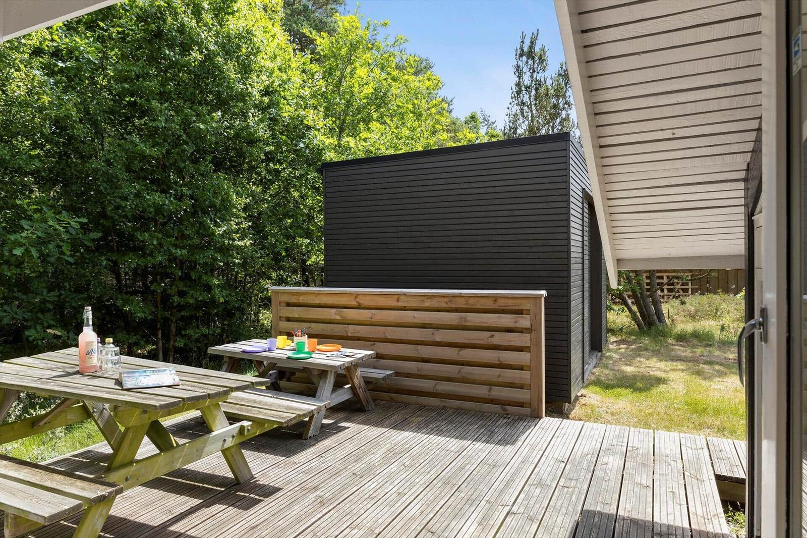 Holzterrasse mit Picknicktisch, Sitzbank und Blick auf einen schwarzen Holzschuppen.