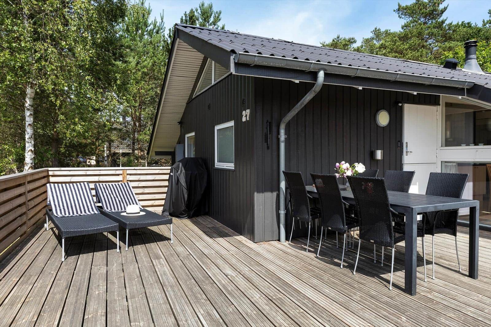 Terrasse mit Tisch, Stühlen und Liegen vor einem Holzhaus.