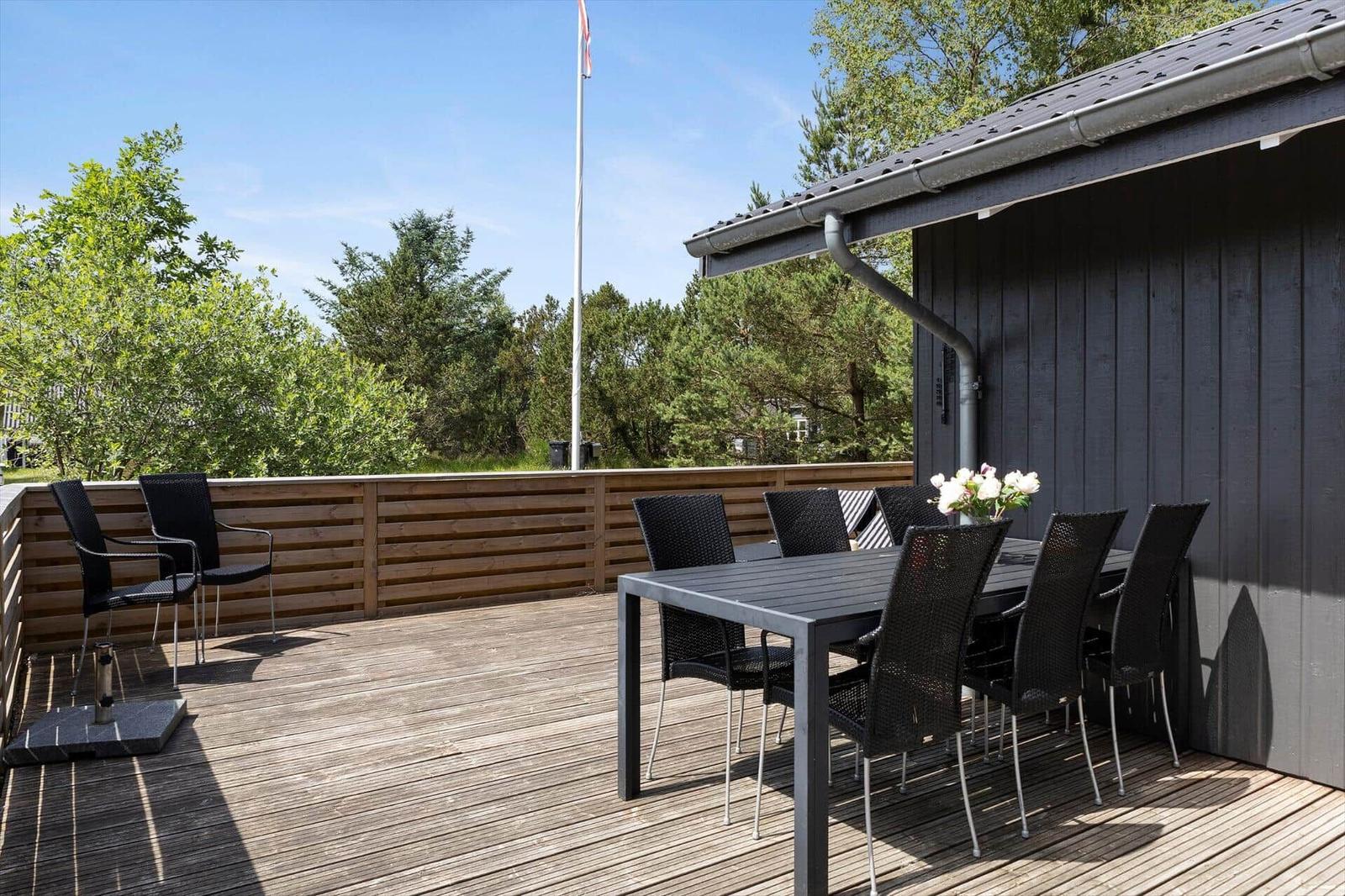 Terrasse mit Tisch und Stühlen, Holzgeländer und Blick auf Bäume.