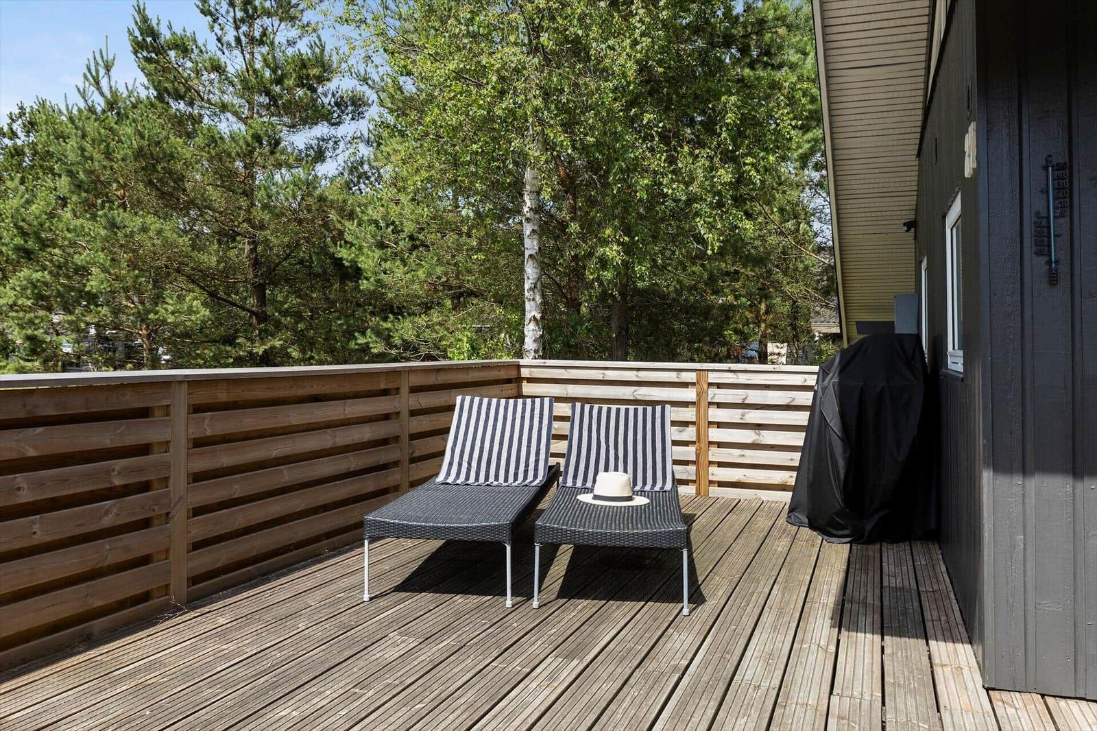Terrasse mit zwei Liegestühlen und Holzgeländer. Hintergrund: Bäume und Hauswand.