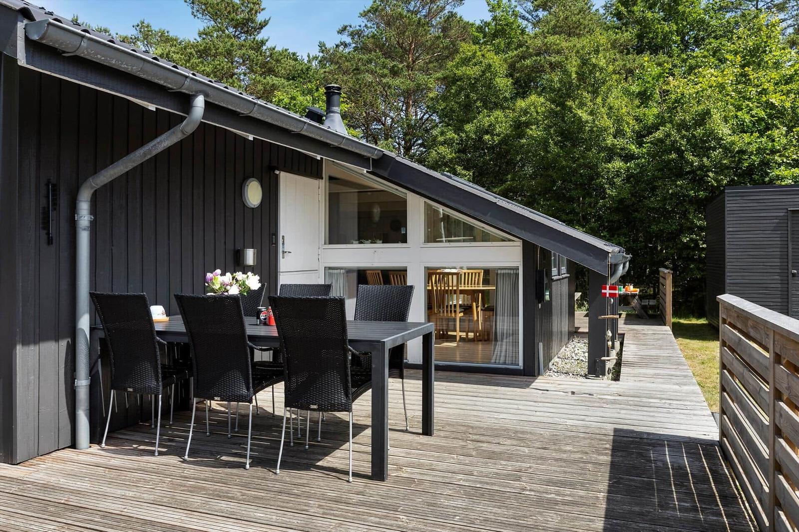 Terrasse mit Tisch und Stühlen vor einem Haus mit großem Fenster.