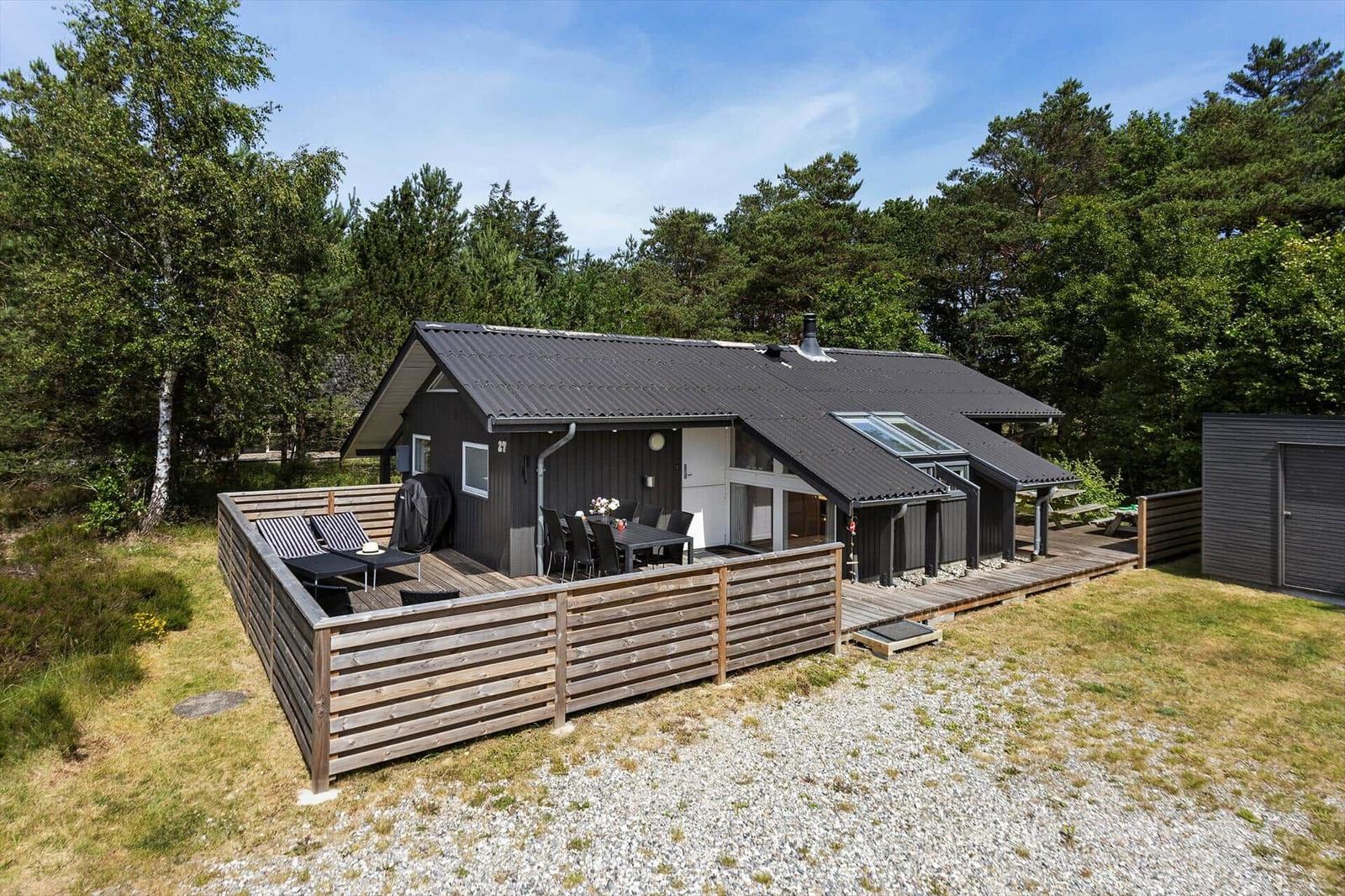 Ein modernes Holzhaus mit Terrasse, Grill und Sitzgelegenheiten im Wald.