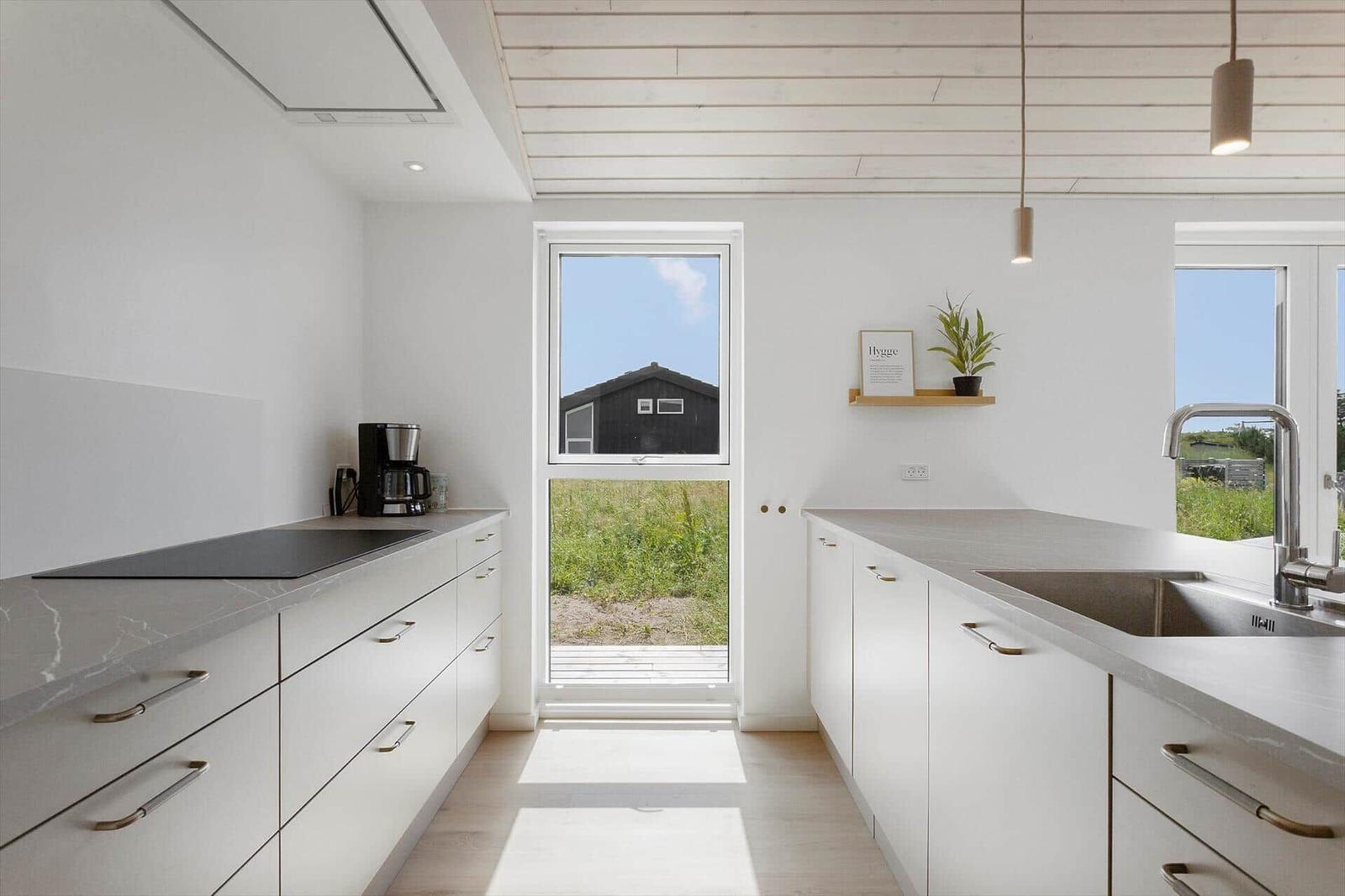 Küche mit weißen Schränken, Steinarbeitsplatte und Fensterblick auf Grünfläche.