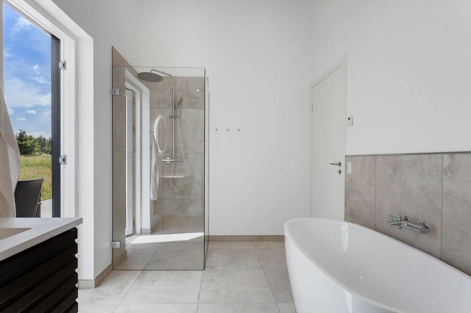 Bad mit Dusche und freistehender Badewanne, großes Fenster mit Blick auf Grünfläche.