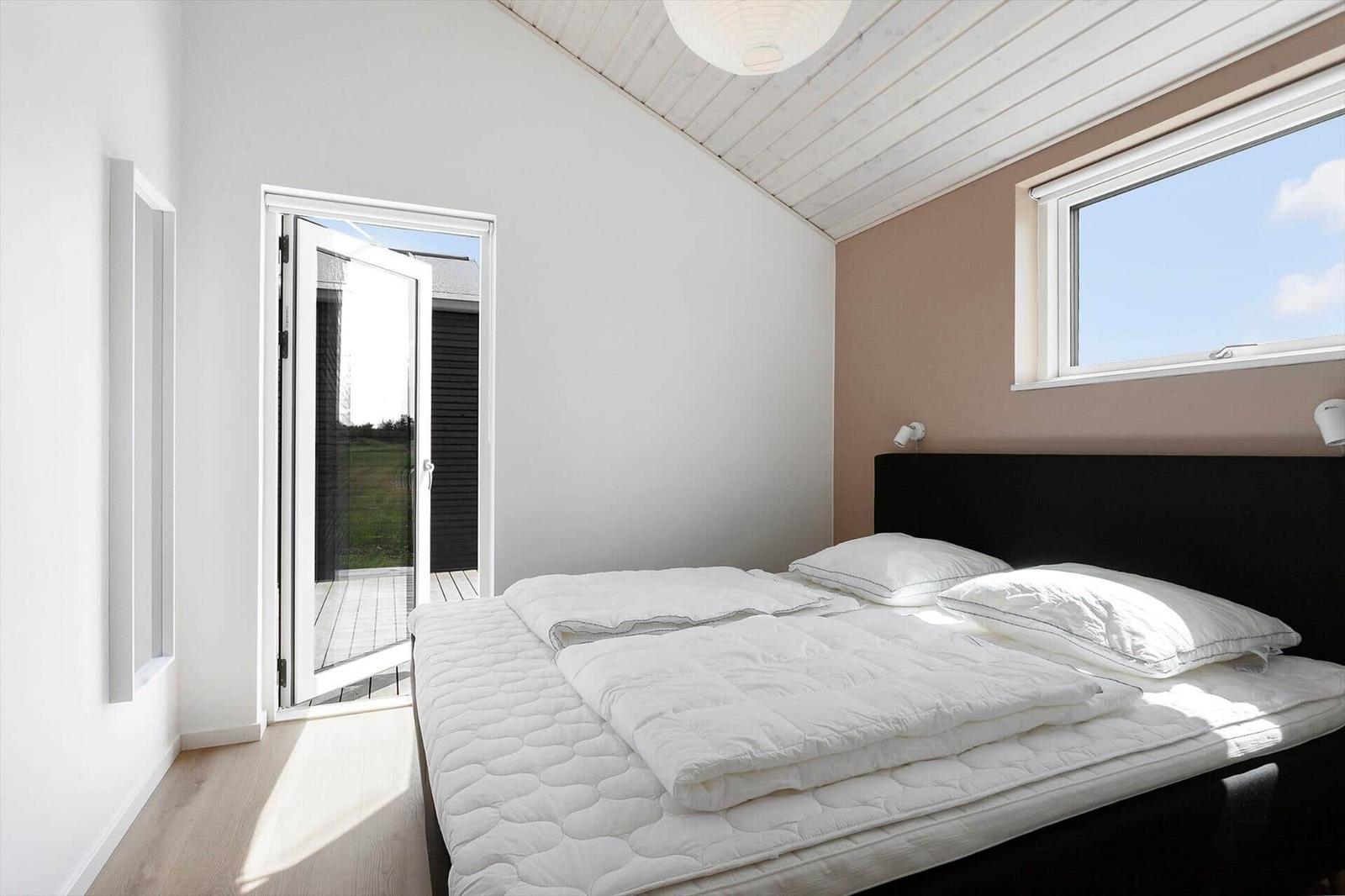 Schlafzimmer mit weißem Bett, Fenster und Tür zum Außenbereich.