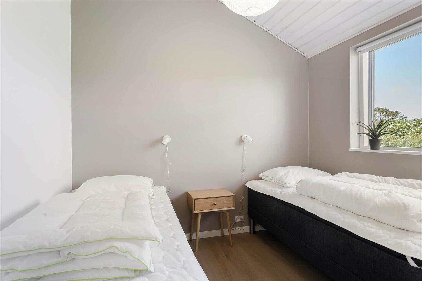 Zwei Betten mit weißen Bettwäsche, Nachttisch und Fenster mit Pflanze.
