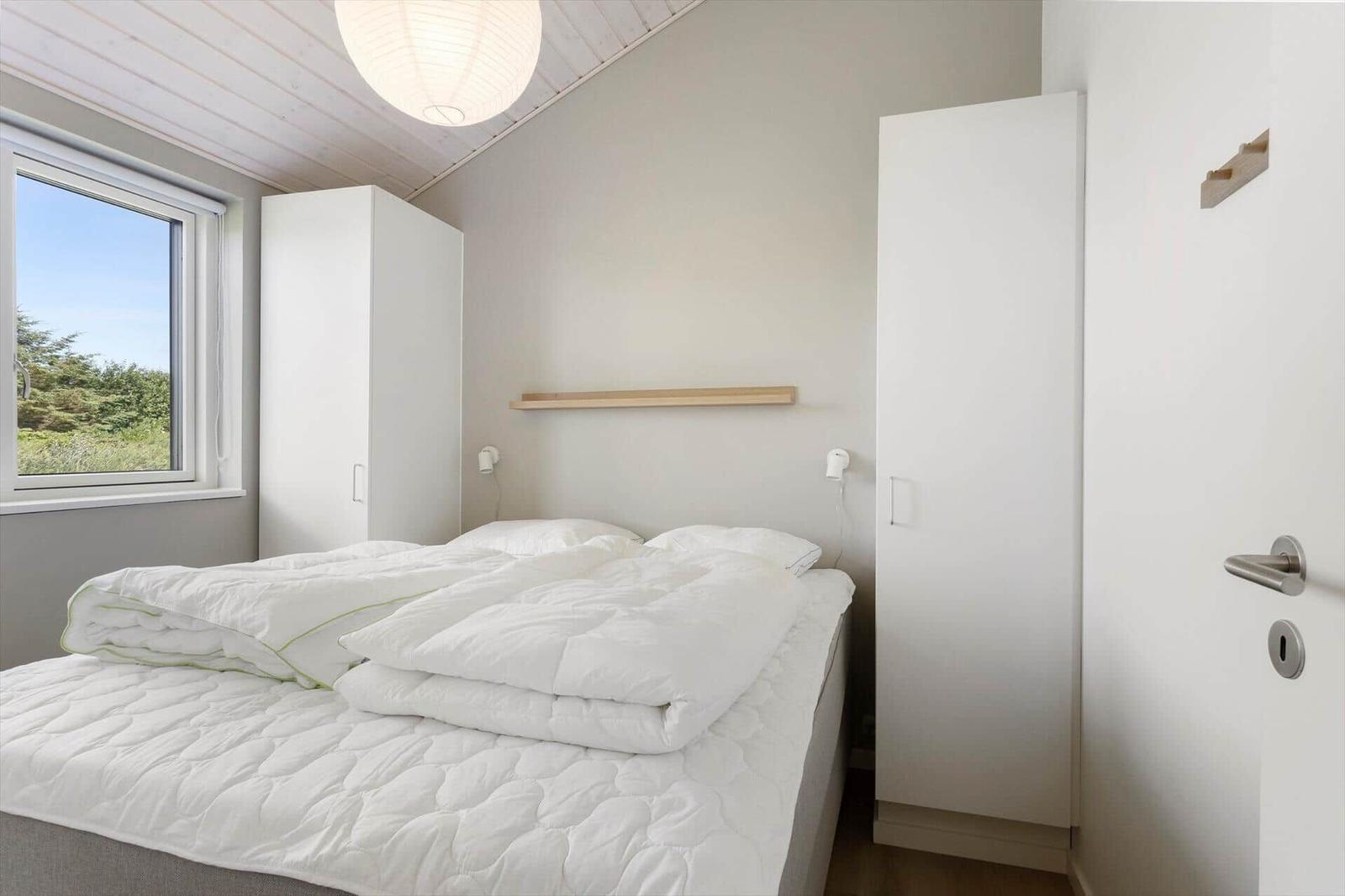 Schlafzimmer mit weißem Bett, Fenster und Schränken.