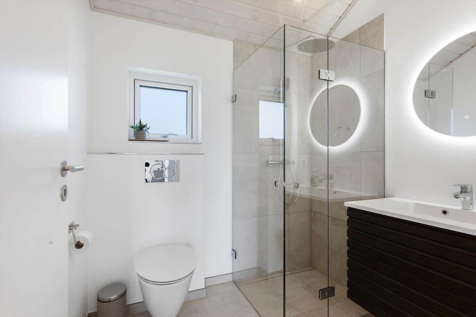 Moderne Badewanne mit Dusche, Waschbecken und Toilette. Ein Fenster mit Pflanze.