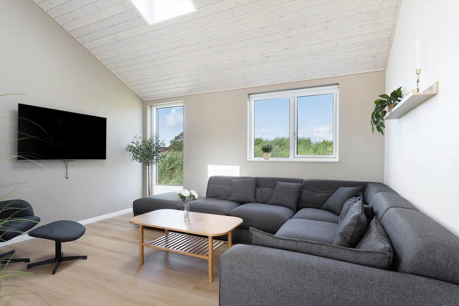 Wohnzimmer mit grauem Sofa, Holztisch und TV an der Wand.