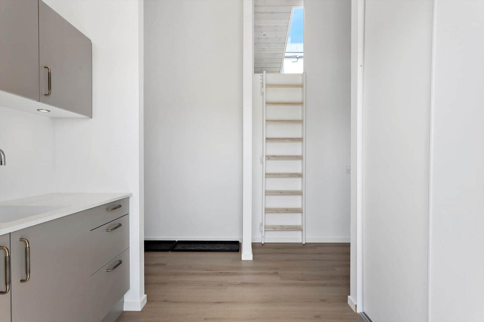 Küche mit grauen Schränken und Holzboden. Treppe führt zu einem Dachboden.