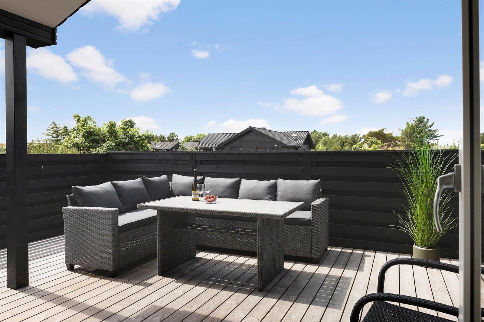 Terrasse mit Sitzgruppe, Tisch und Pflanze. Hintergrund: Holzzaun und Häuser.