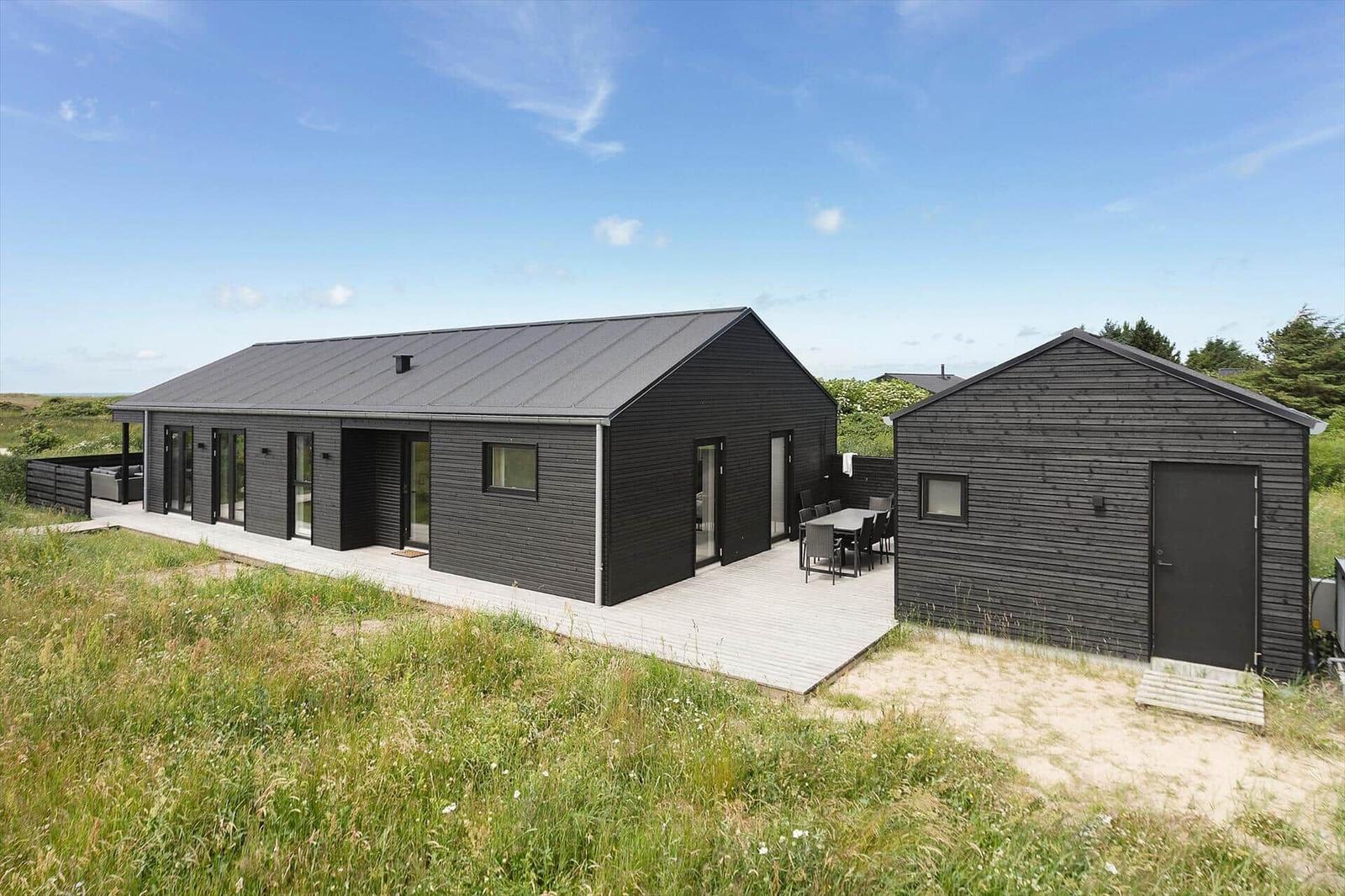 Moderne schwarze Holzhütte mit Terrasse und Garten. Außentisch und Sitzgelegenheiten.