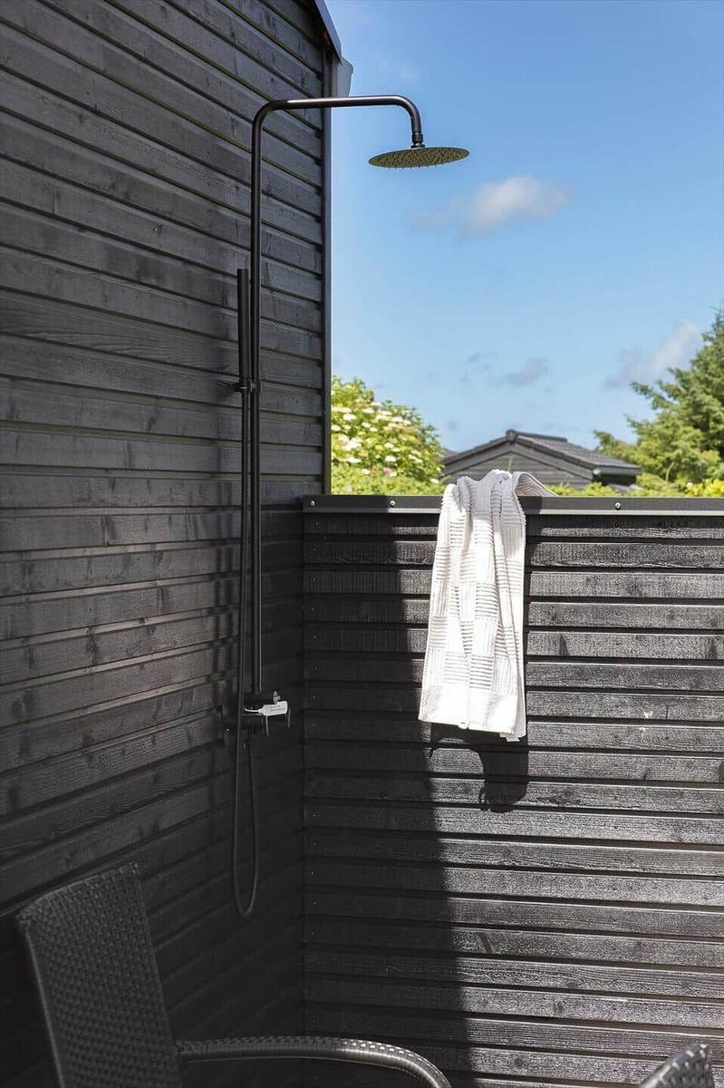 Außen-Dusche mit Duschbrause an schwarzer Holzwand. Handtuch hängt an der Wand.