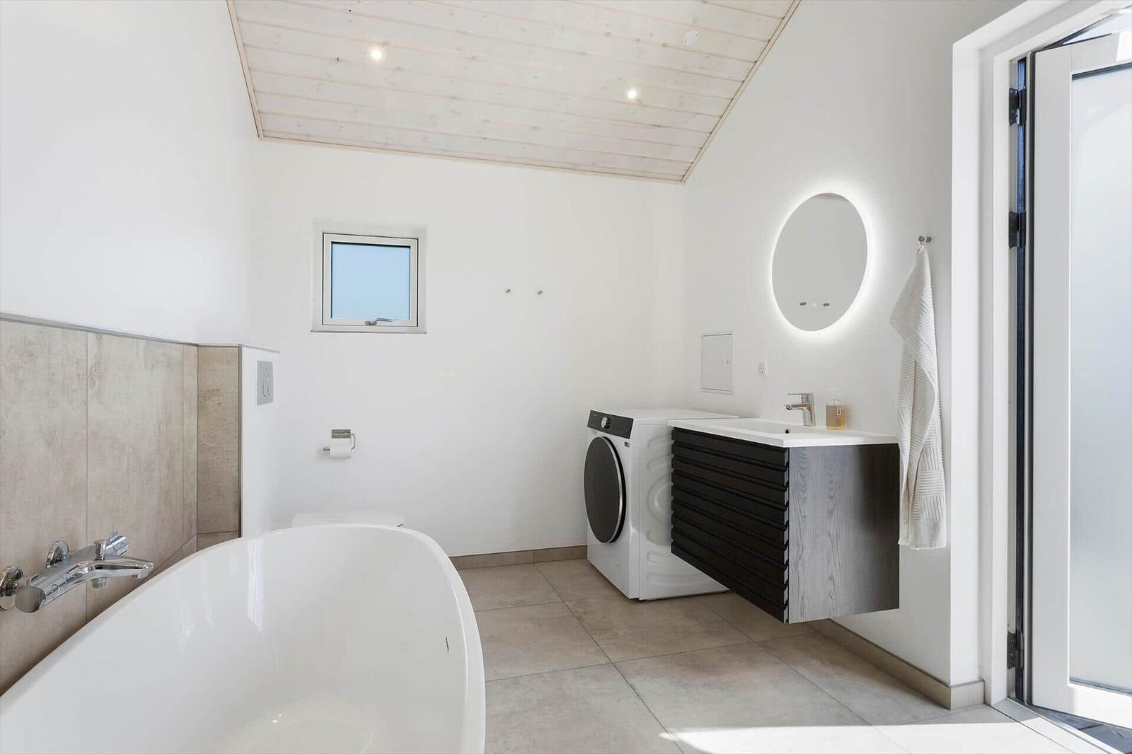 Badezimmer mit freistehender Badewanne, Waschmaschine und beleuchtetem Spiegel.