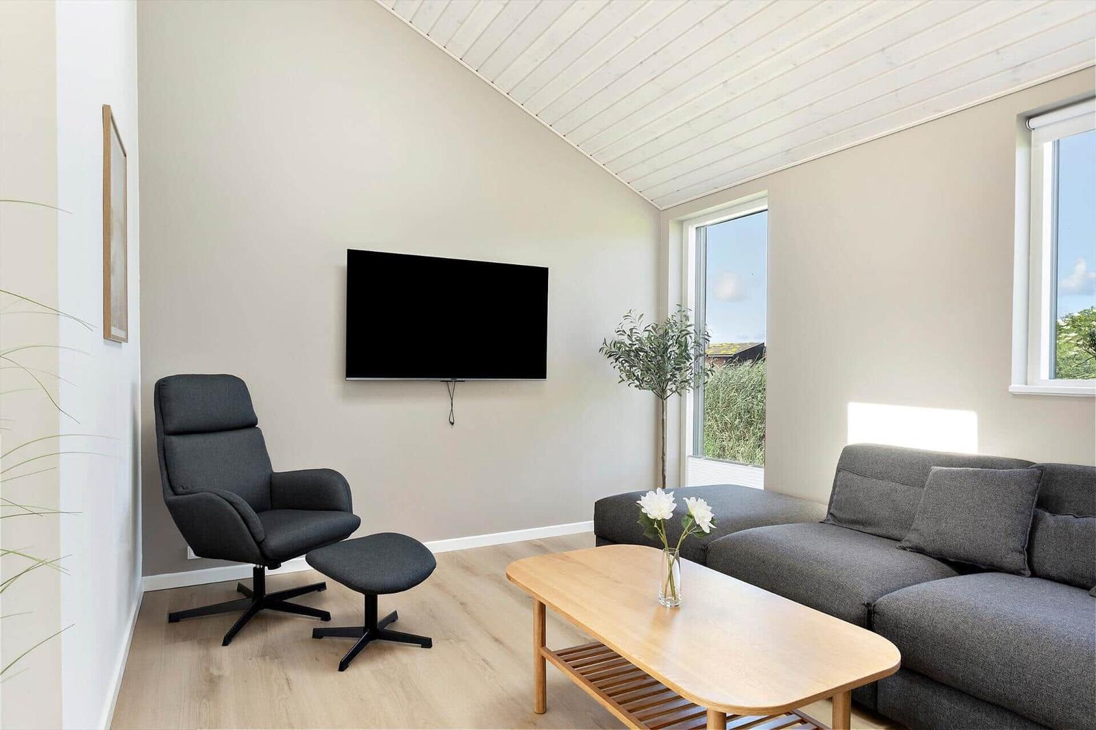 Wohnzimmer mit Sofa, Sessel, Fernseher und Holztisch.