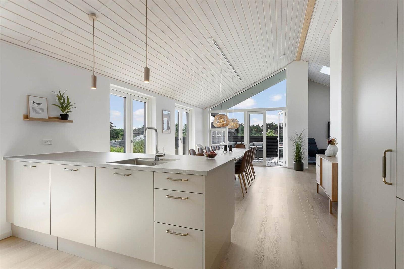 Küche mit Insel, Glasfront und Lichtern. Holzboden und weiße Wände.