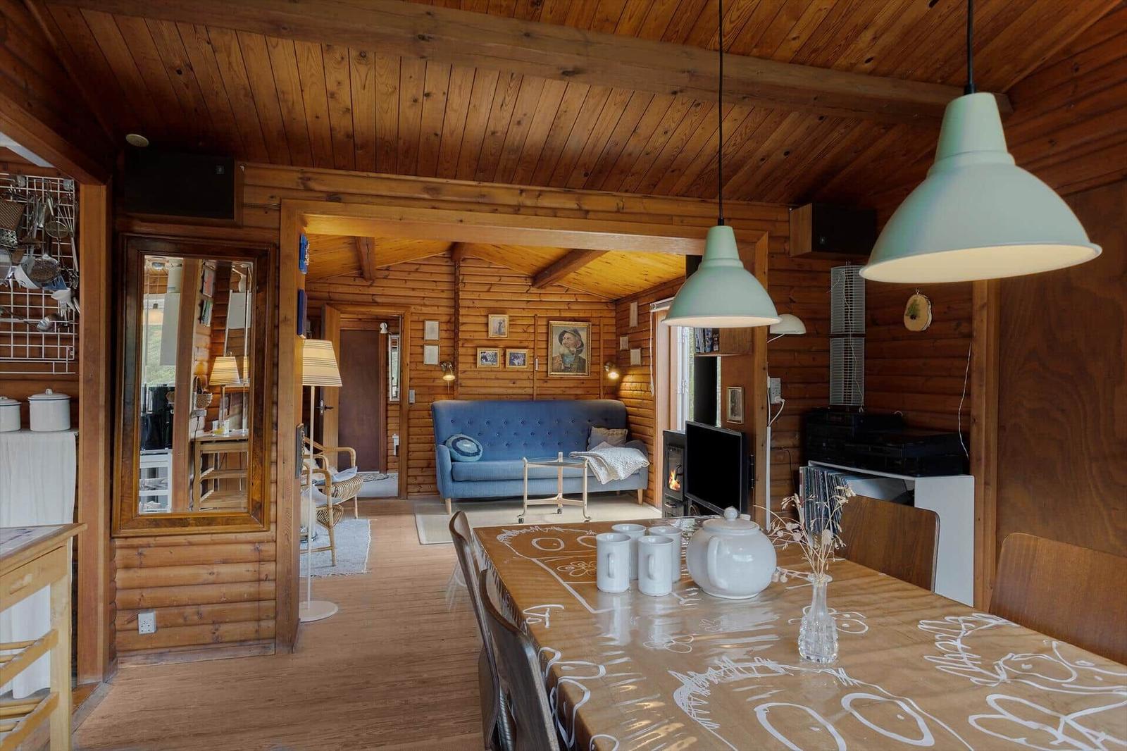 Esszimmer mit Holzwand und Tisch, Wohnzimmer mit Sofa und Kamin im Hintergrund.