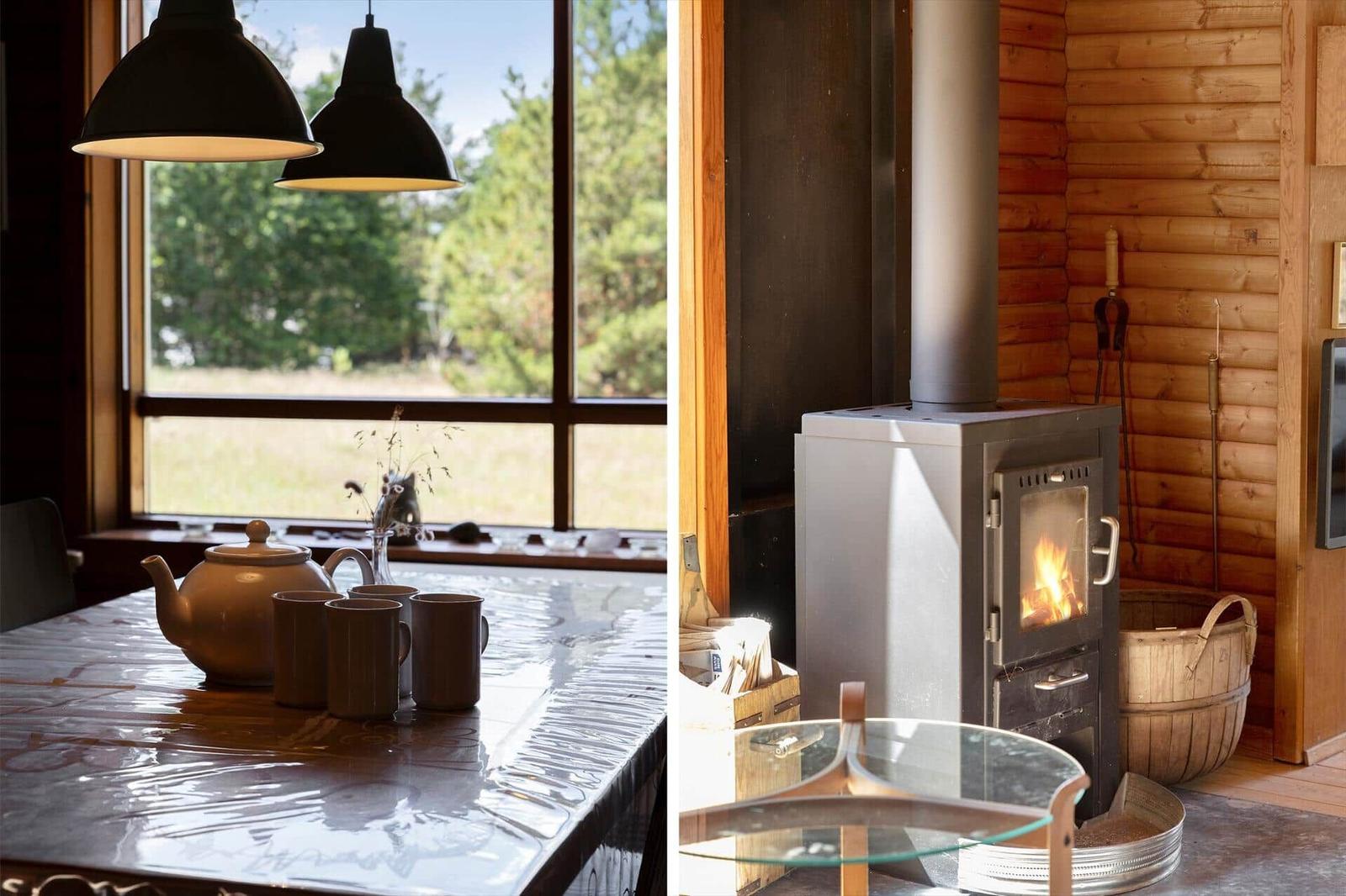 Tisch mit Teekanne und Tassen vor großem Fenster. Holzofen mit brennendem Feuer in rustikalem Raum.