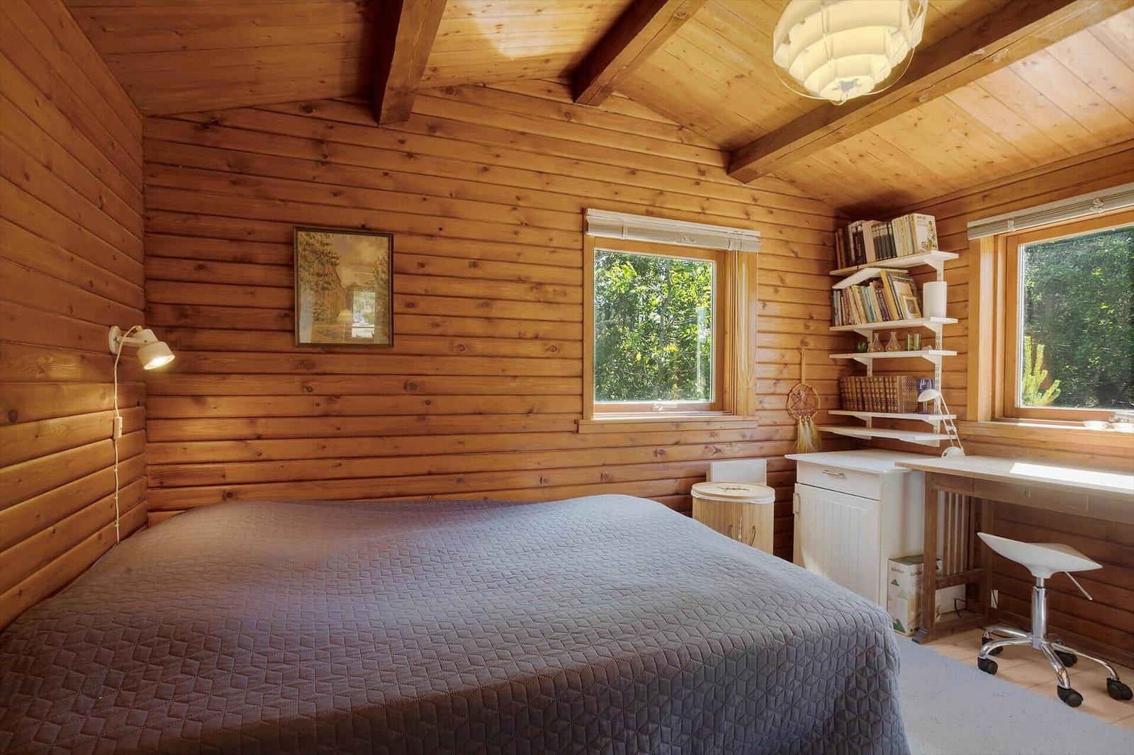 Schlafzimmer mit Holzwand, Bett, Schreibtisch und Fenstern.