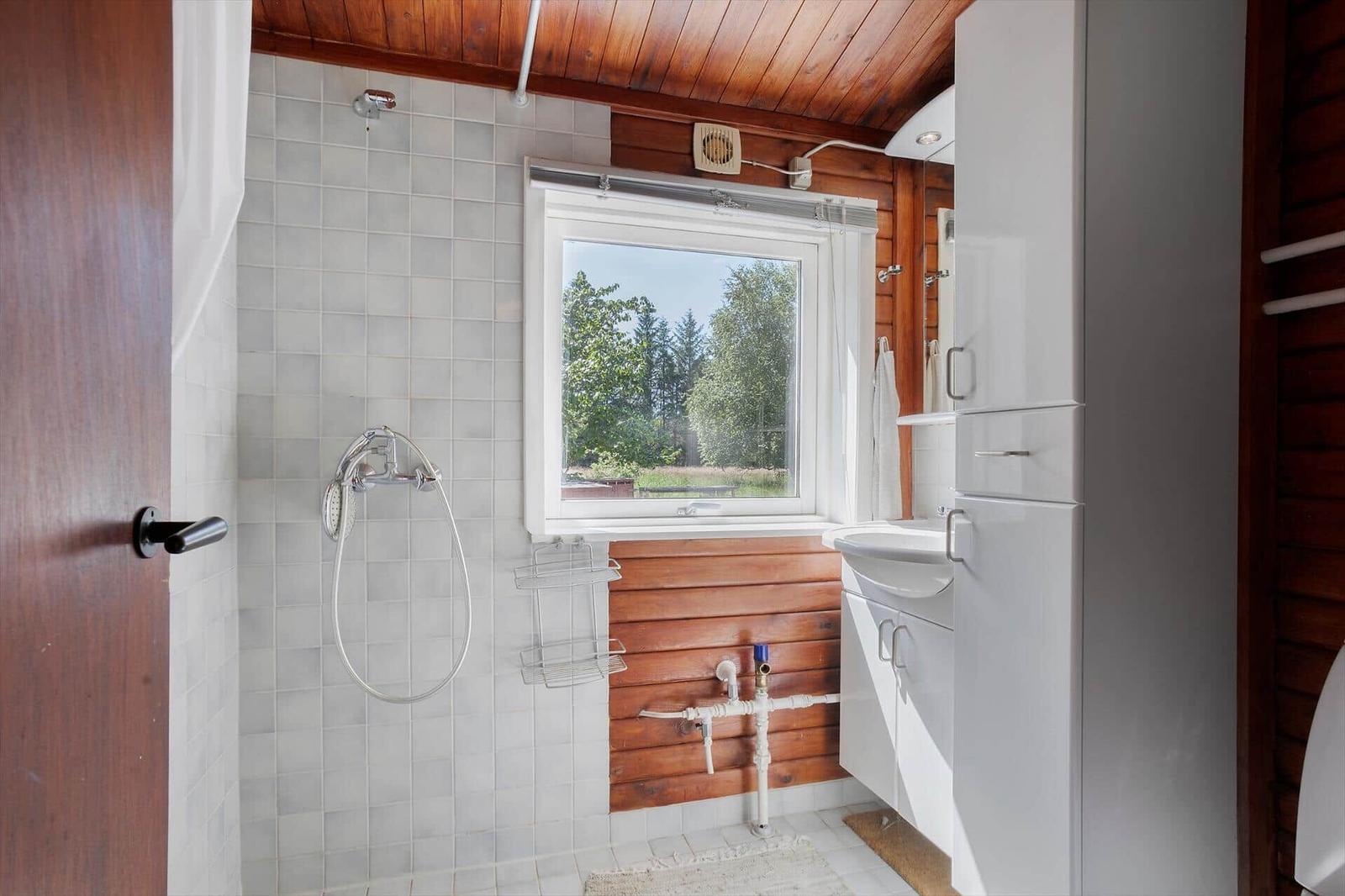 Badezimmer mit Dusche, Waschbecken und Fenster zum Wald