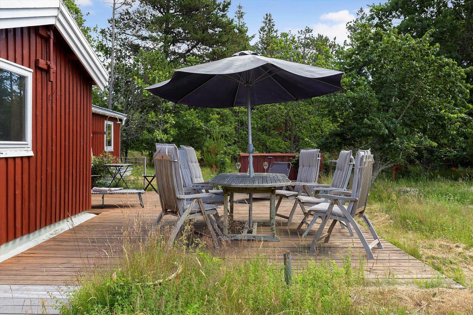 Holzterrasse mit Tisch, Stühlen und Sonnenschirm neben rotem Haus.