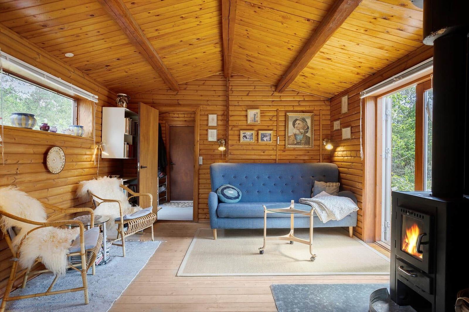 Wohnzimmer mit Holzwand, blauem Sofa, Kamin und Fenstern zum Blick in die Natur.