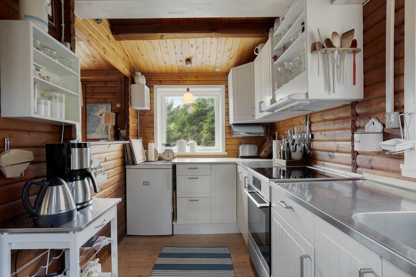 Küche mit weißen Schränken, Holzwänden und Fensterblick auf Wald.