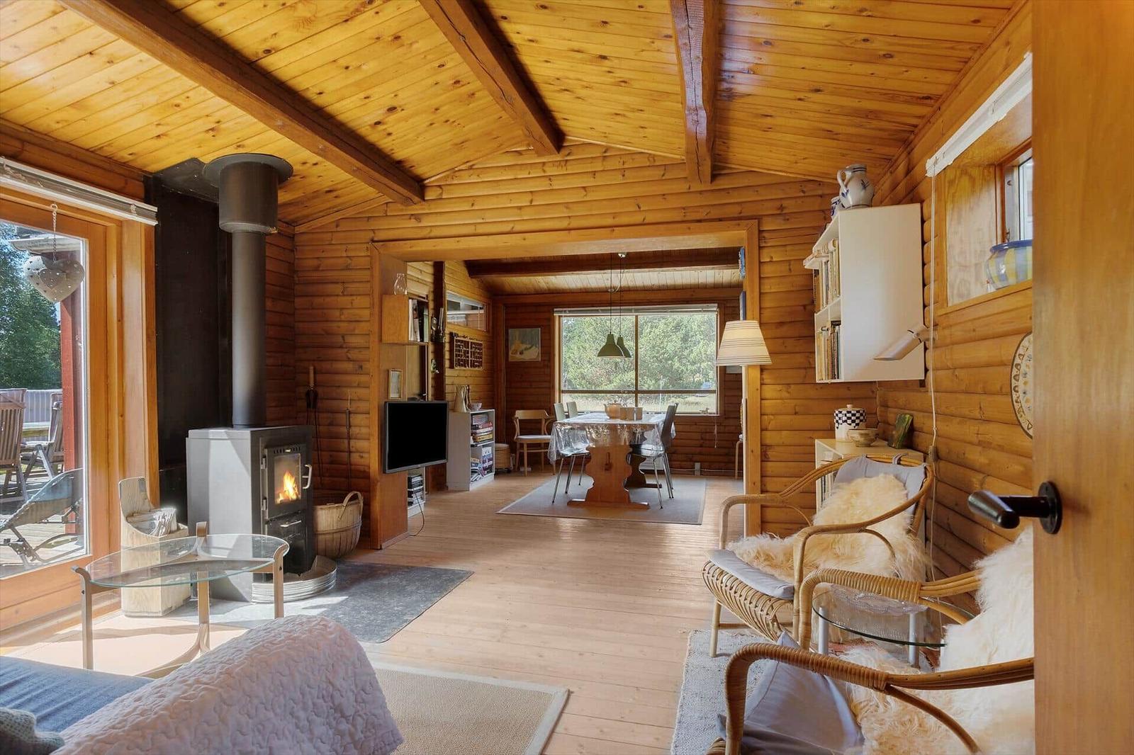 Wohnraum mit Holzdecke, Kamin und Sitzgelegenheiten. Essbereich mit Tisch und Stühlen.