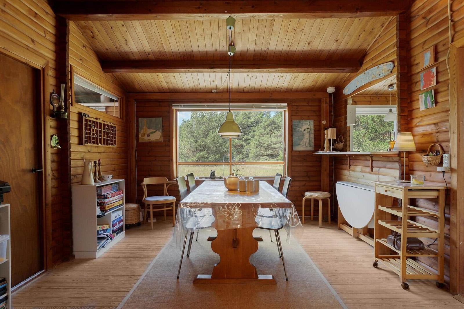 Esszimmer mit Holzwand, Tisch, Stühlen und Fensterblick auf Wald.