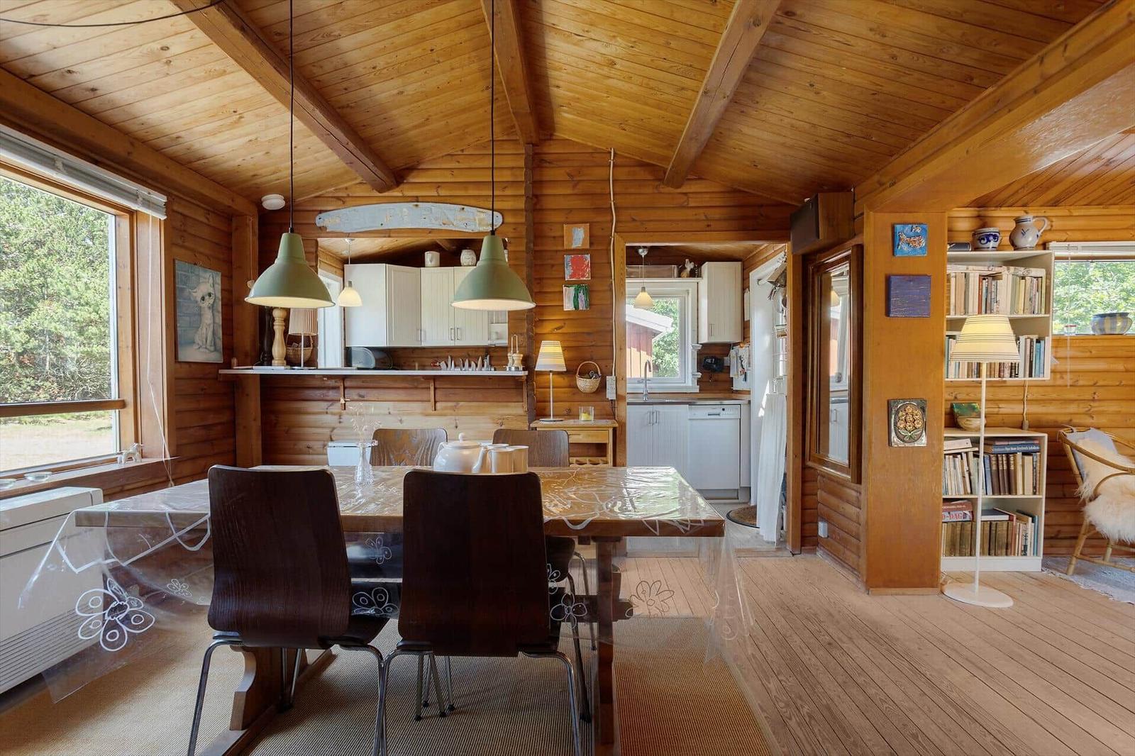 Esszimmer mit Holzdecke, Tisch und Stühle. Küche und Wohnbereich sichtbar.